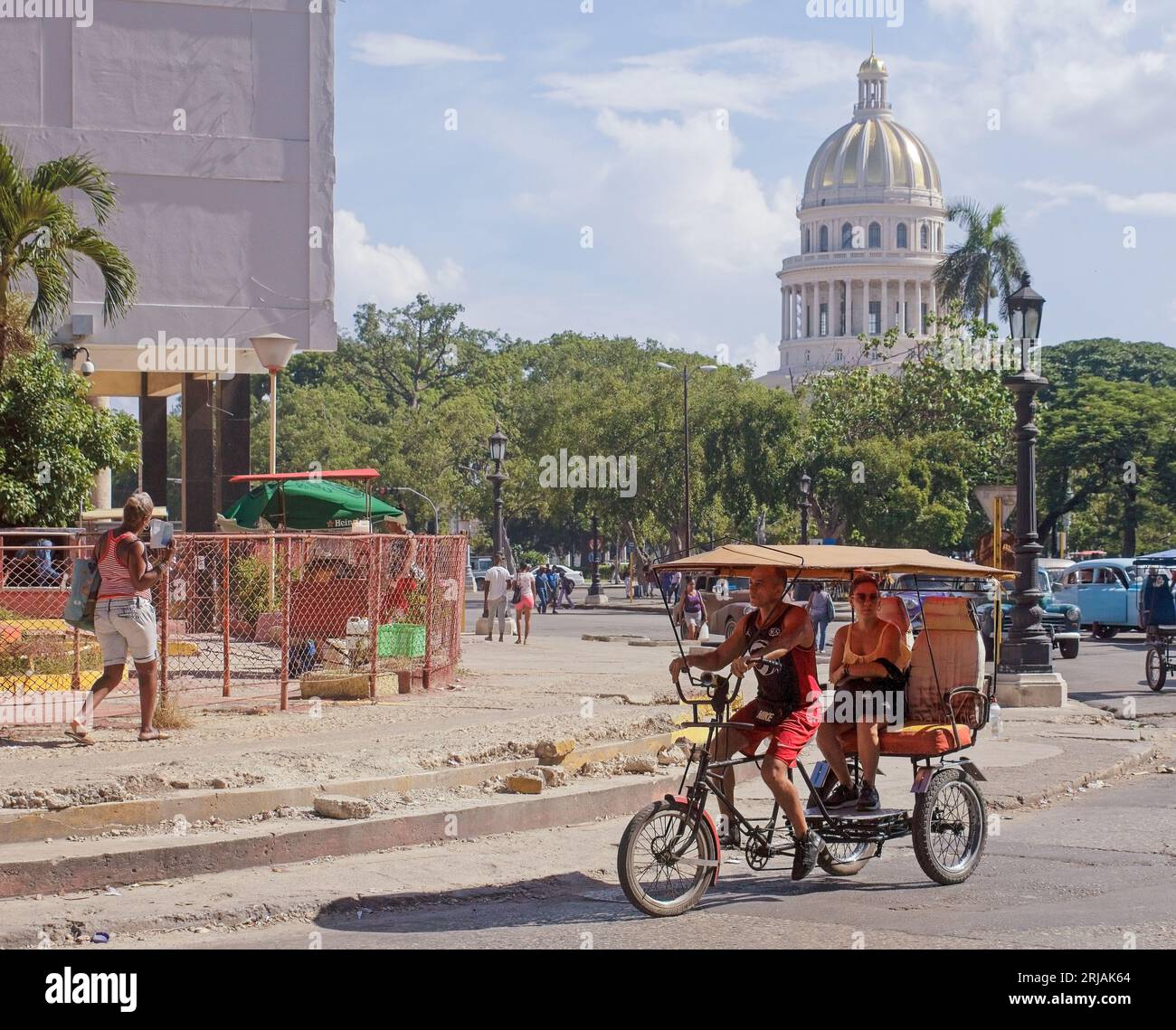La Havane, Cuba, un bicitaxi ou un pédicab conduit dans un coin de ville. Le bâtiment Capitolio est en arrière-plan. Banque D'Images