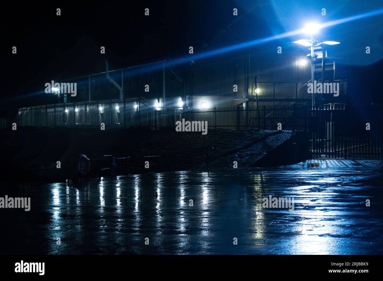 Une scène pluvieuse montrant les lumières d'un bâtiment de jetée se reflétant sur l'asphalte humide d'un parking Banque D'Images
