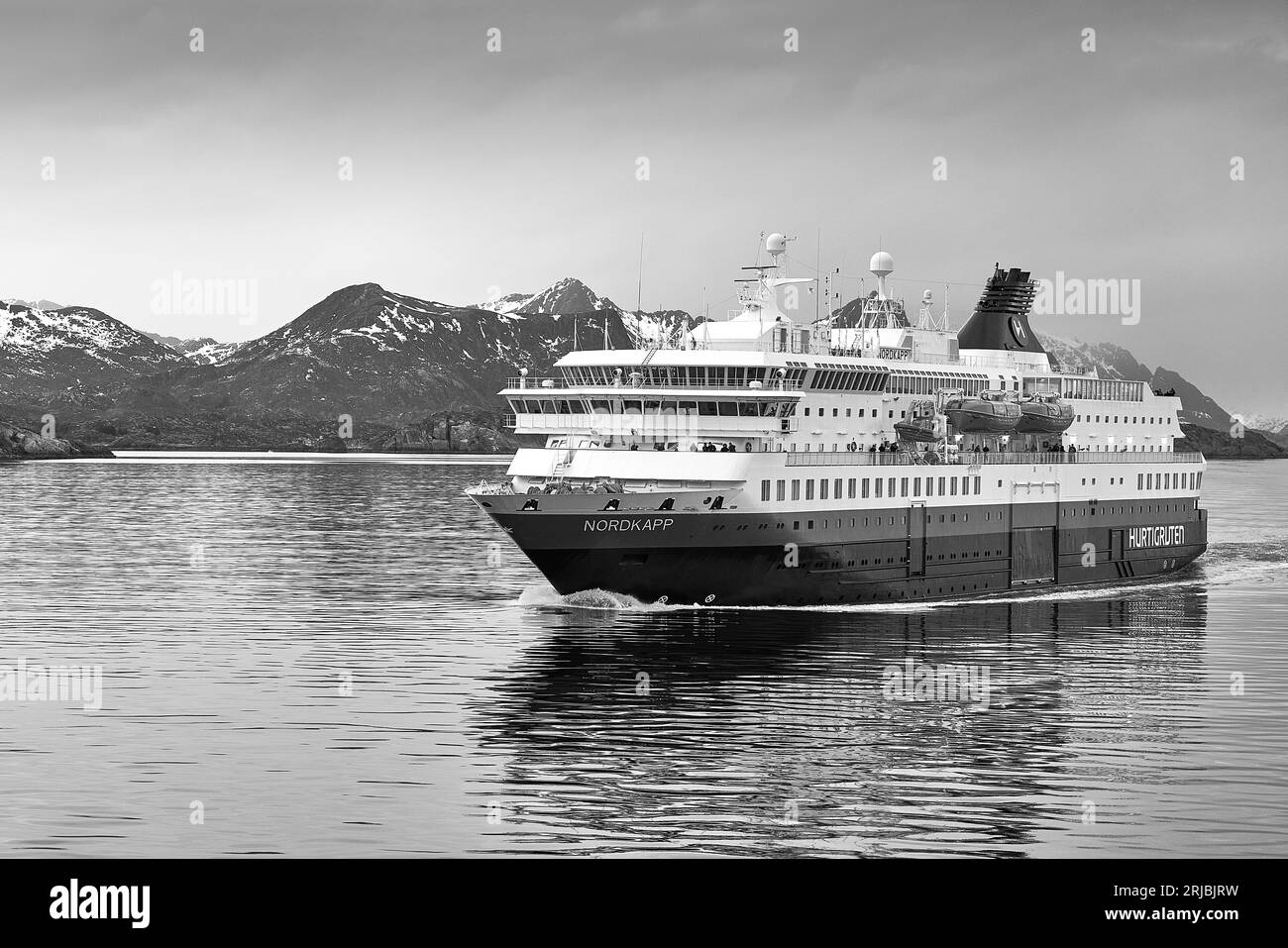 Noir et photo du ferry norvégien Hurtigruten, MS NORDKAPP, fuyant de Svolvaer, derrière les montagnes enneigées des îles Lofoten Banque D'Images