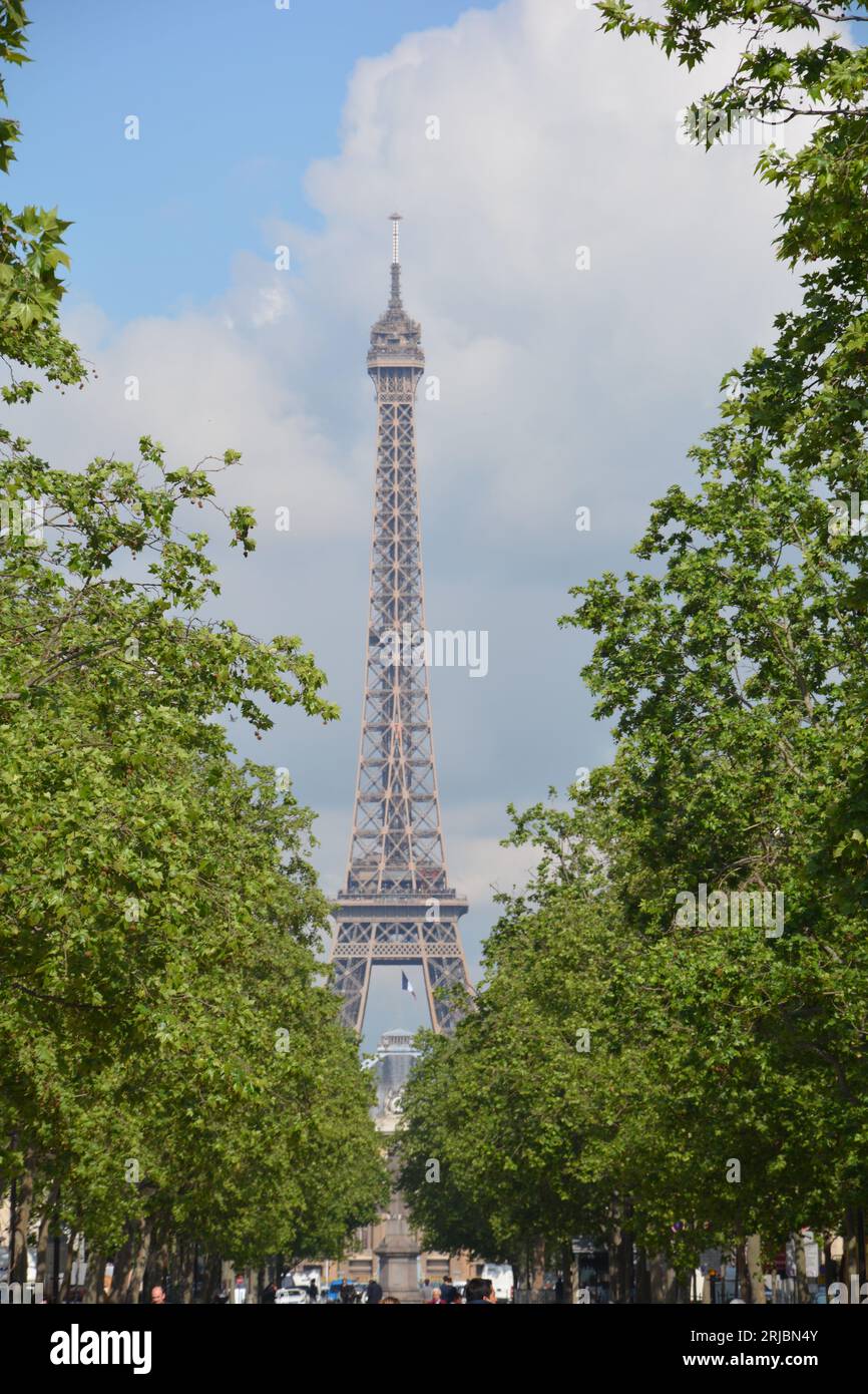 Vue sur la Tour Eiffel à travers les arbres par temps clair avec un ciel bleu clair et quelques nuages blancs. Prise de vue du champ de Mars Banque D'Images