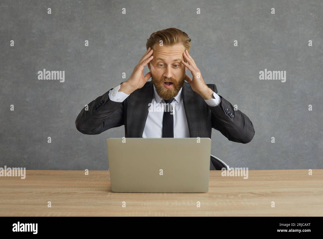 Choqué et confus homme d'affaires caucasien attrape sa tête tout en regardant l'écran d'ordinateur portable. Banque D'Images