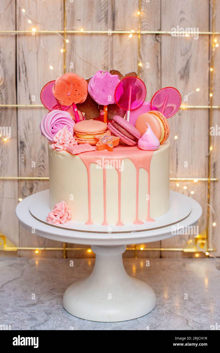 Gâteau blanc avec chocolat fondu rose, meringues et sucettes sur fond festif Banque D'Images