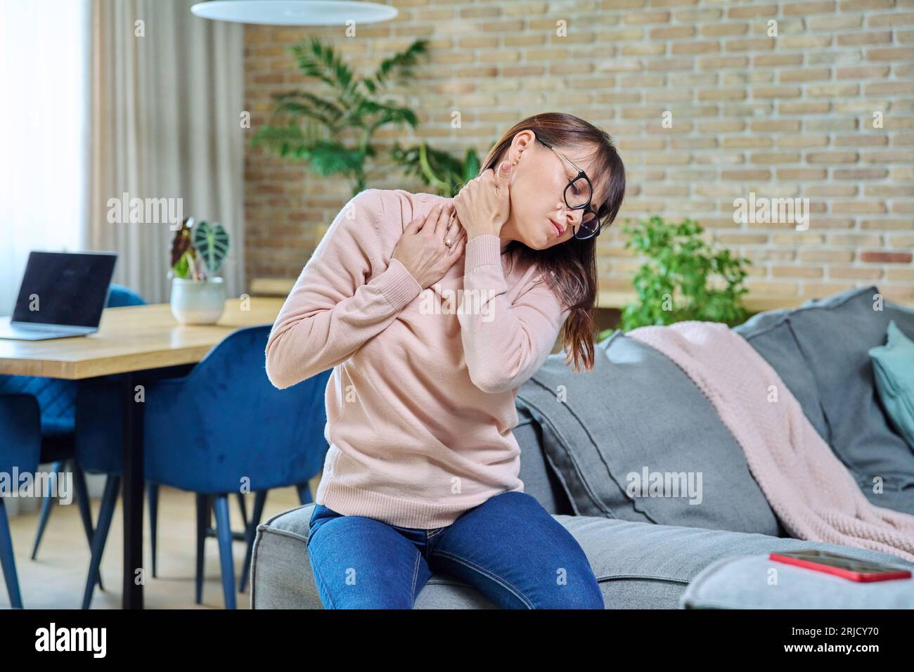 Douleur dans le cou dérangeant femme d'âge moyen, femme souffrant assise à la maison Banque D'Images