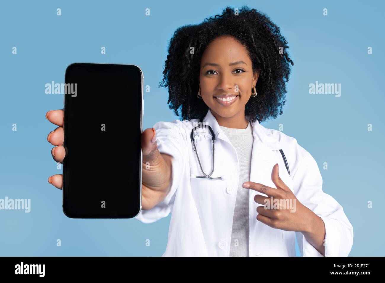Positif noir Millennial dame médecin dans le doigt blanc de point de manteau au smartphone avec écran vide Banque D'Images