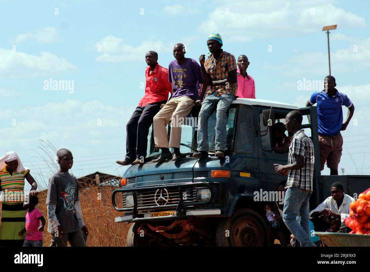 Des hommes sont vus assis sur le dessus d'un camion garé regardant un spectacle aérien de loin à Mt Hampden, Zimbabwe. Banque D'Images