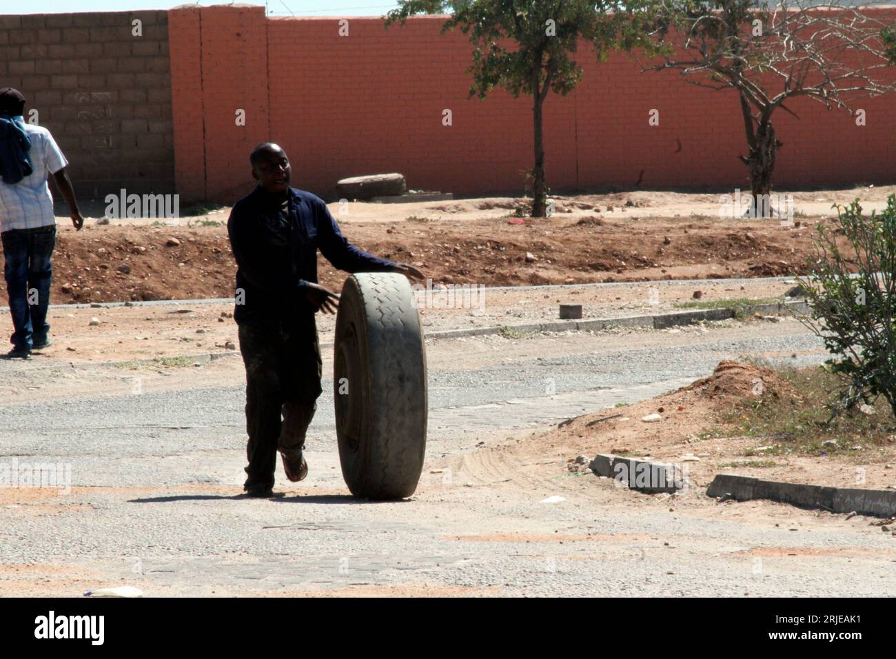 Un homme poussant un gros pneu vers une station-service à Beitbridge. La ville de Beitbridge est une plaque tournante de l'activité des camions, car les camions circulent entre l'Afrique du Sud et le Zimbabwe. Banque D'Images