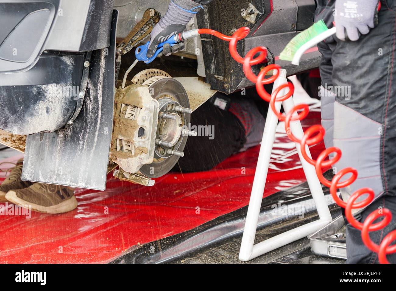 Entretien de la voiture de rallye dans le parc de service, soufflant de la boue et de la saleté du disque de frein et de l'étrier avec de l'air comprimé Banque D'Images
