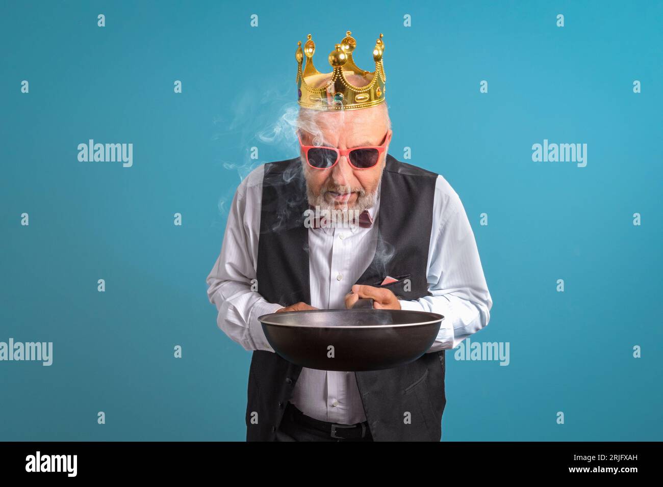 Roi de la cuisine. Un homme en couronne d'or avec une poêle brûlée à la main. Sur fond bleu Banque D'Images