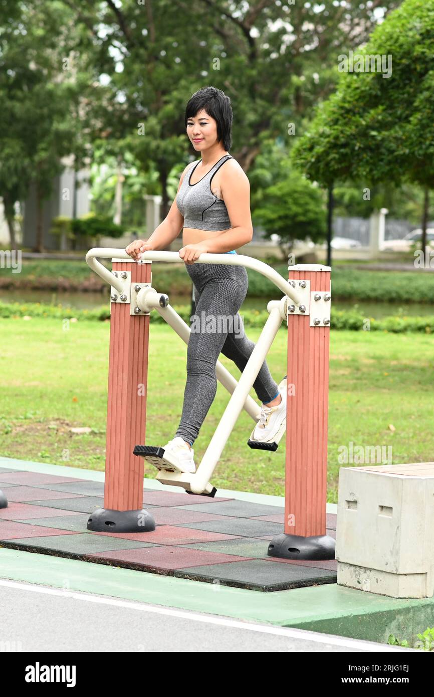 Jolie femme asiatique faisant de l'exercice sportif avec un type de machine d'exercice balançant les jambes dans le parc extérieur. Banque D'Images