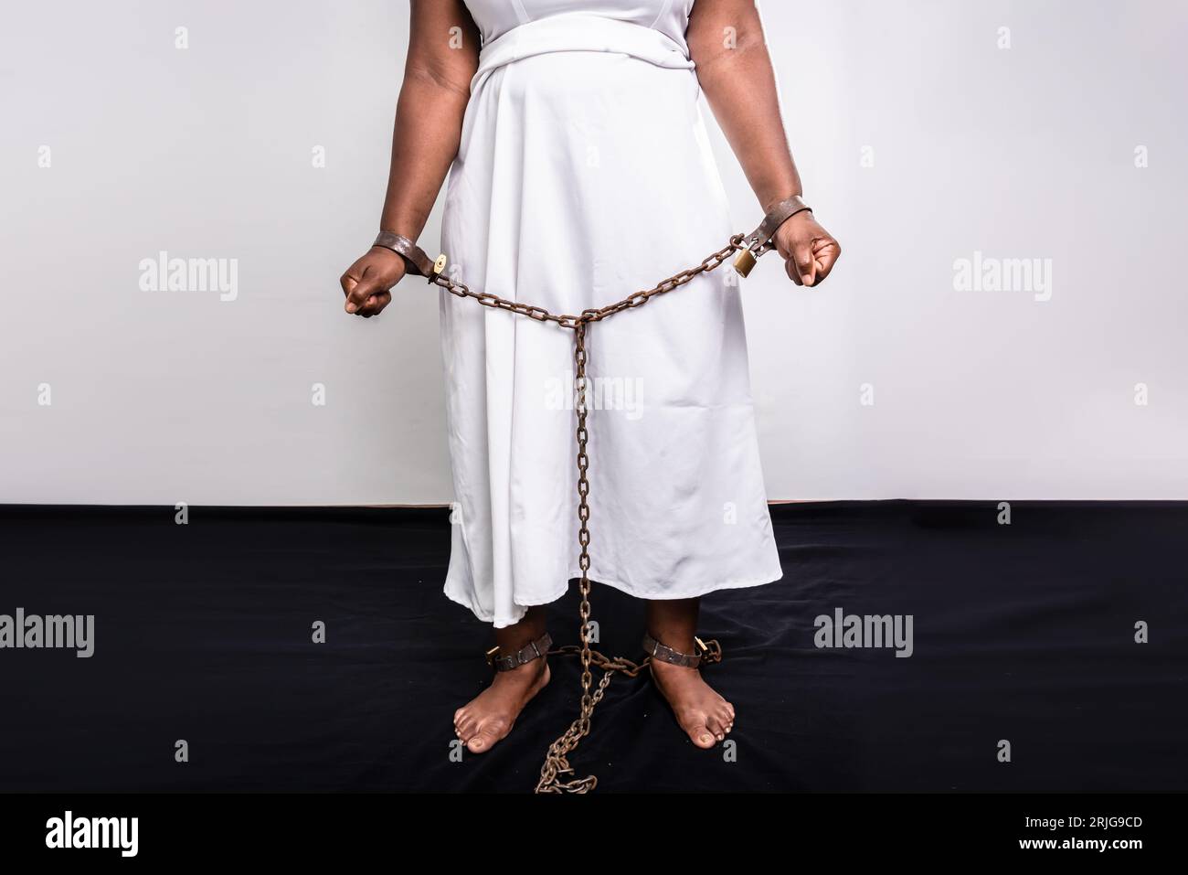 Mains et jambes d'une femme noire enchaînée avec une ancienne chaîne en fer rouillé et un cadenas. Concept de prévention du commerce des esclaves. Banque D'Images