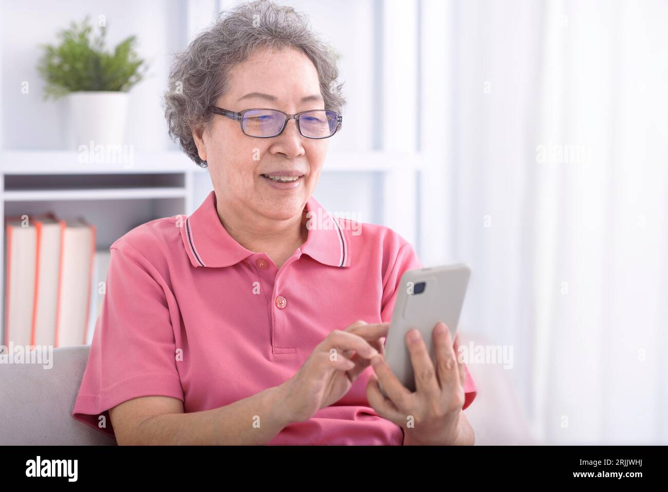 Femme âgée assise sur le canapé et naviguant sur le téléphone portable Banque D'Images