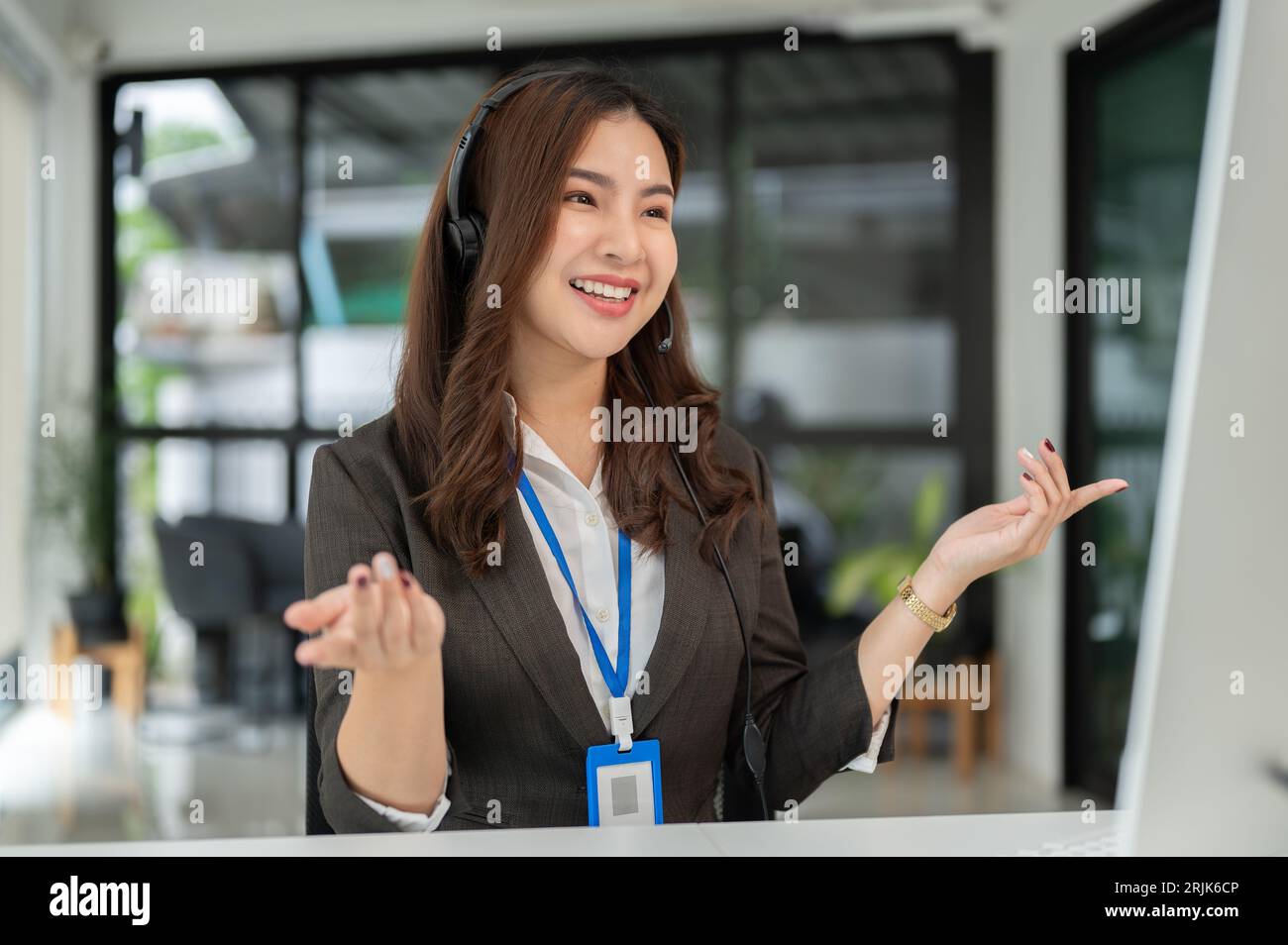 Un agent de centre d'appels ou un opérateur de télévendeur asiatique attrayant et joyeux avec un micro-casque sans fil offre une expérience client positive Banque D'Images