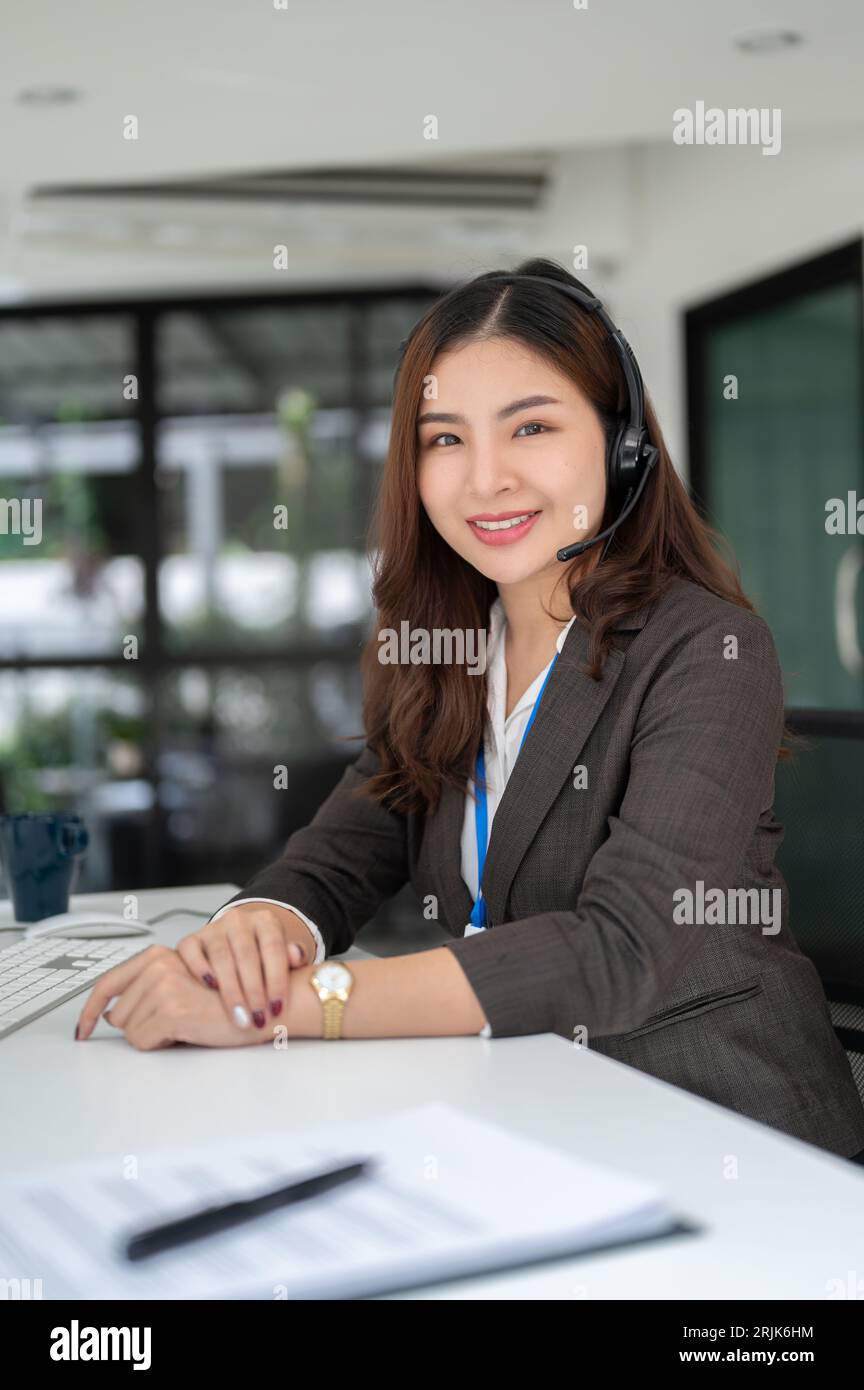 Portrait d'une charmante agente de vente asiatique ou d'une opératrice de centre d'appels avec un micro-casque assis à son bureau et regardant la caméra. télémarketing, cust Banque D'Images
