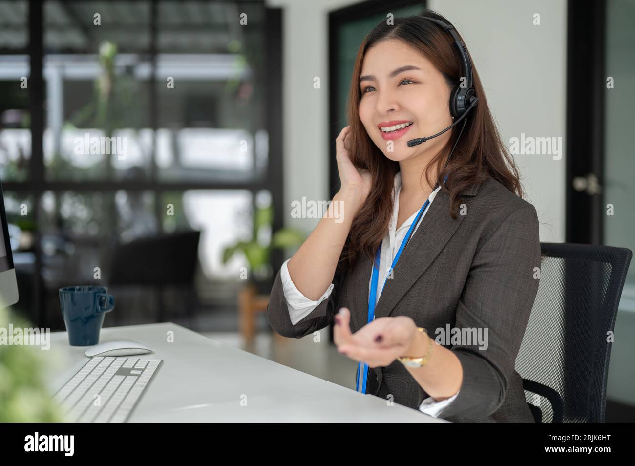 Une opératrice de centre d'appels asiatique professionnelle et charmante avec un micro-casque travaille à son bureau, conseille et fournit une expérience client positive Banque D'Images