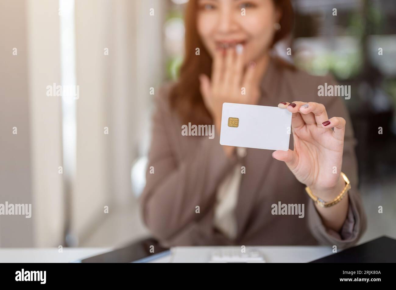 Image rapprochée d'une femme asiatique choquée et excitée montrant une carte de crédit ou de débit à l'appareil photo alors qu'elle était assise à une table. Banque D'Images