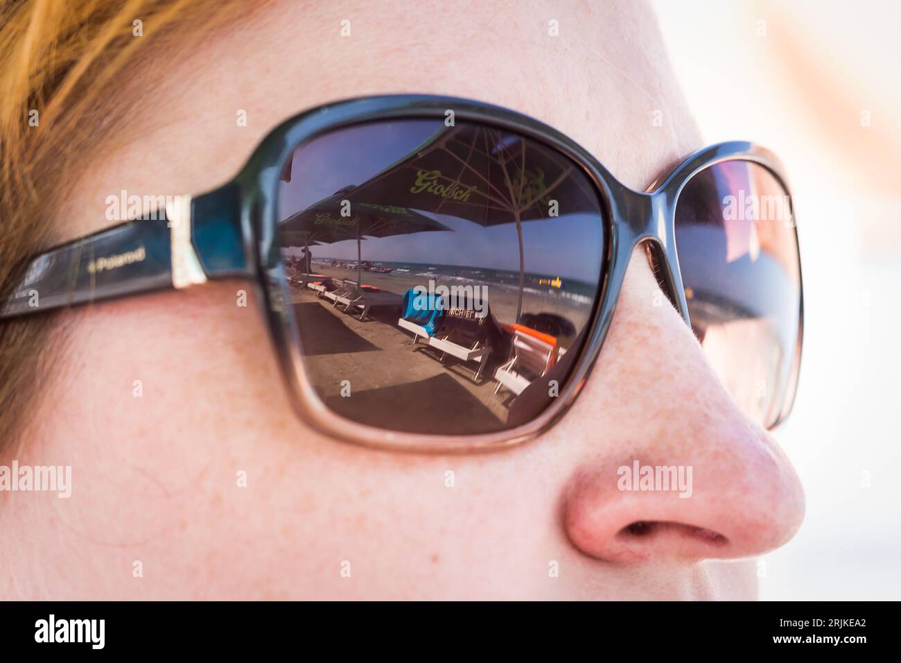 Une femme portant des lunettes de soleil miroir à la mode se tient à l'extérieur lors d'un événement, examinant plusieurs voitures dans les environs Banque D'Images