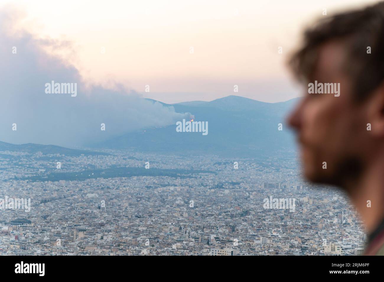 Le 22/08/2023 un feu de forêt a commencé sur les contreforts de la montagne Parnitha dans la banlieue ouest d'Athènes, Grèce. Alimentée par des vents violents, elle a rapidement grandi et brûlé des maisons et des commerces. Cette photo est de la colline de Lycabette, où les touristes et les habitants regardent le feu. Banque D'Images