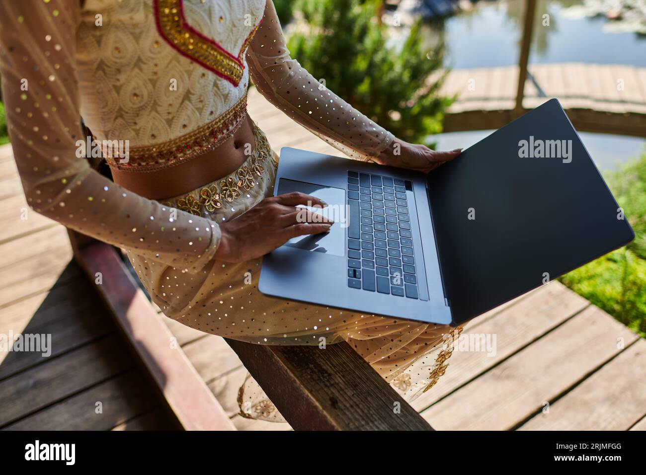 vue recadrée de la femme indienne dans le réseau de vêtements traditionnels, en utilisant un ordinateur portable dans le parc d'été Banque D'Images