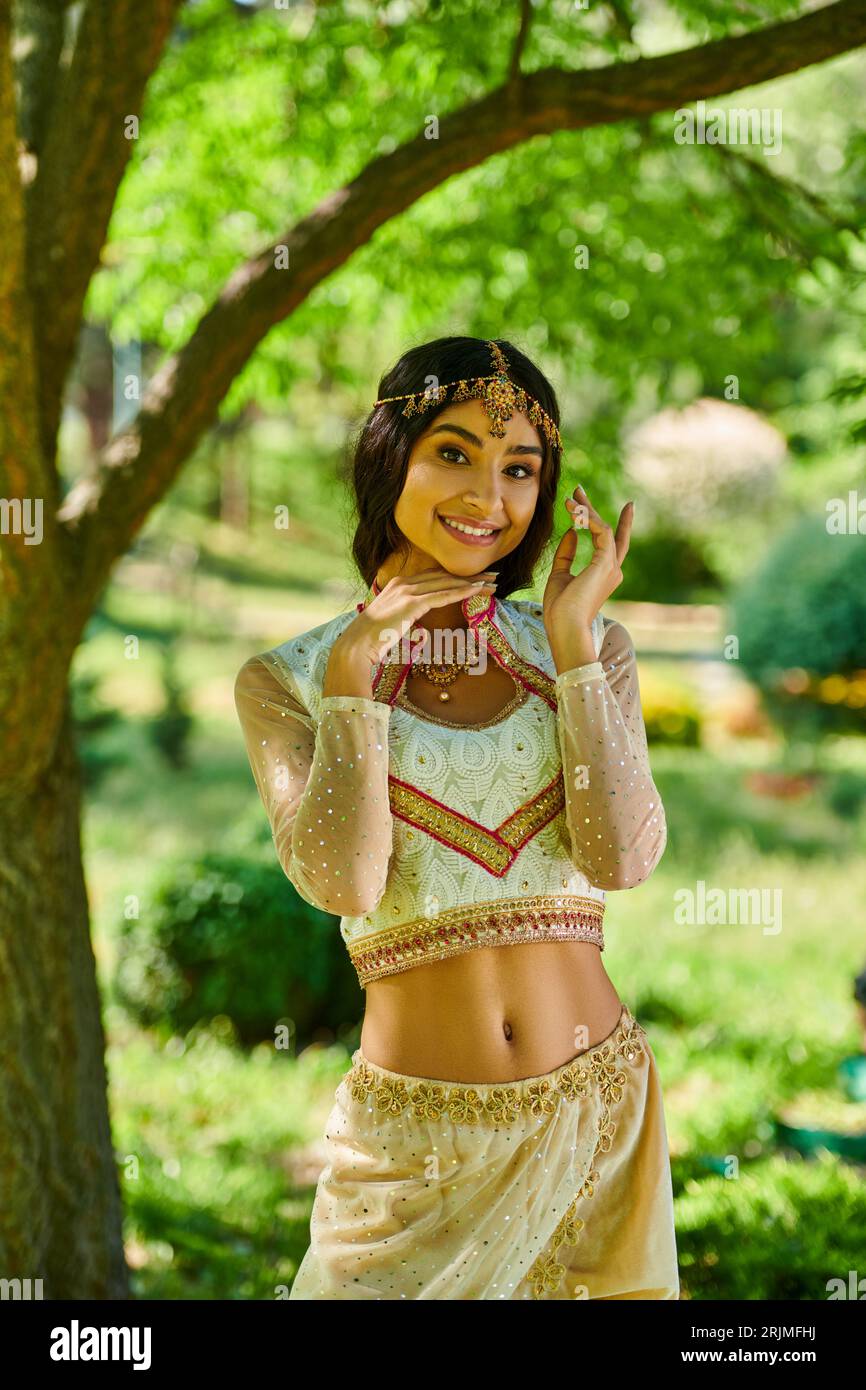 mode traditionnelle, été, femme indienne heureuse debout dans le parc vert et regardant la caméra Banque D'Images