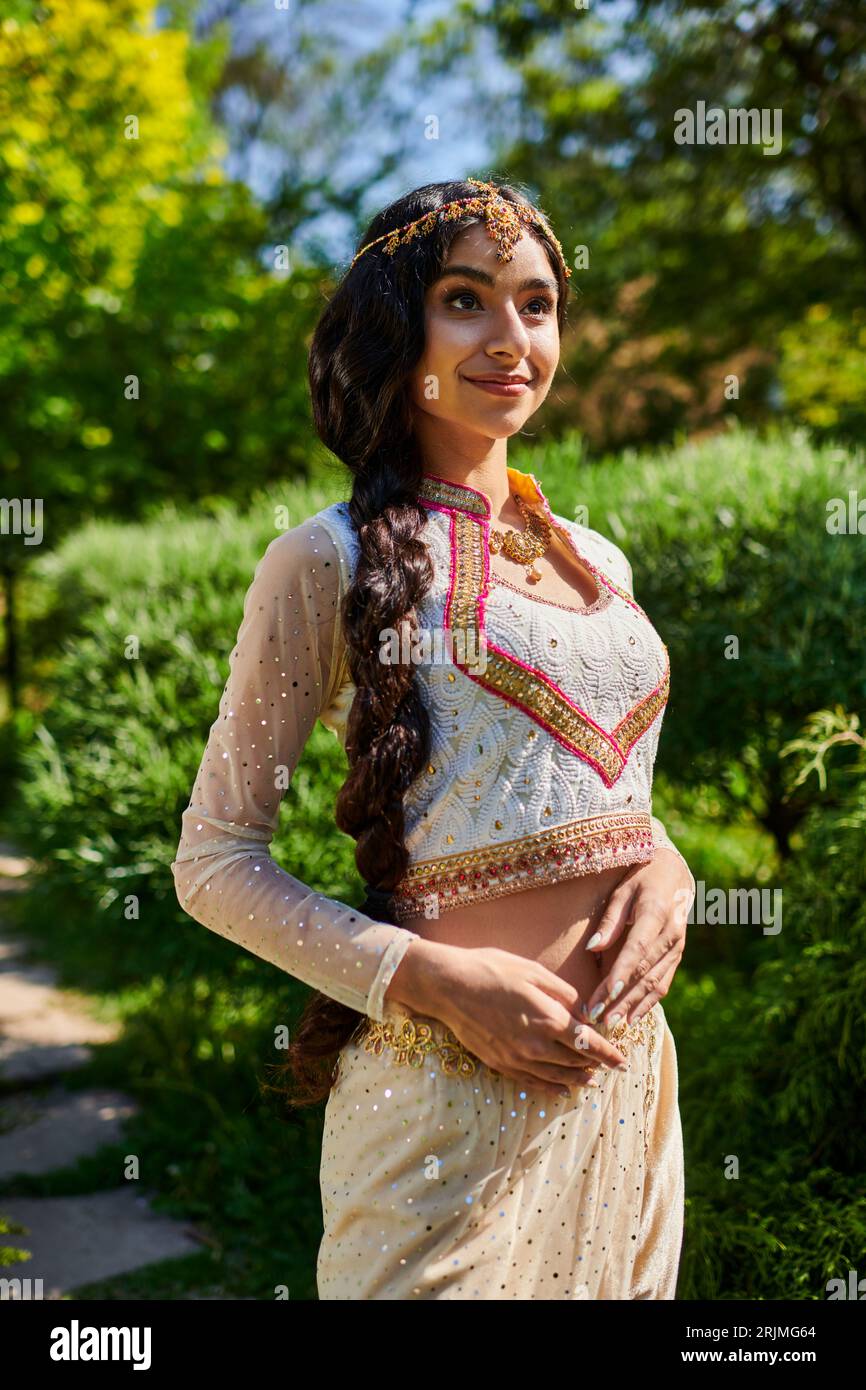 élégante et jeune femme indienne en tenue traditionnelle tendance debout et posant dans le parc Banque D'Images