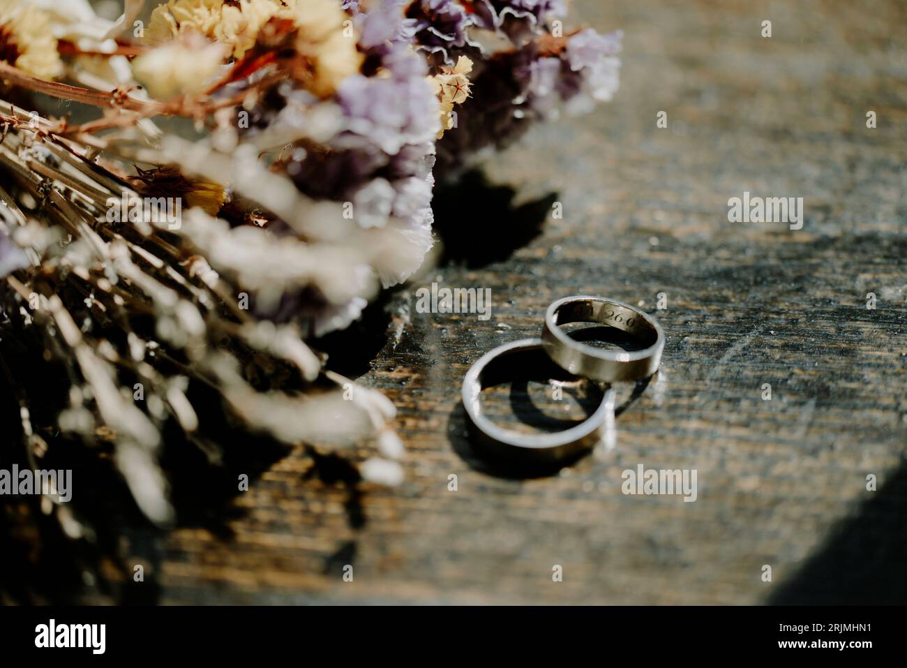 Les anneaux de mariage reposant près d'un paquet de fleurs roses séchées sur une table en bois Banque D'Images