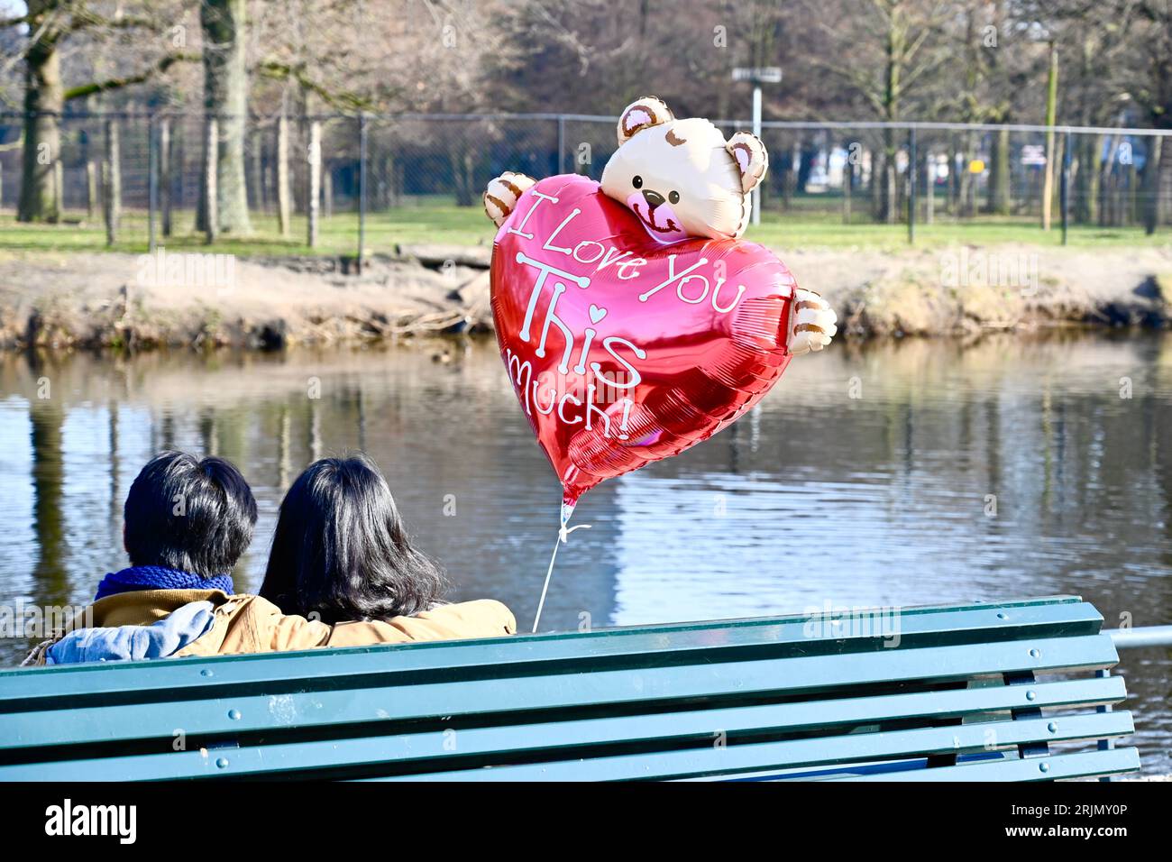 Couple amoureux ensemble sur un banc de ville, tenant un ballon "Je t'aime tellement" Banque D'Images