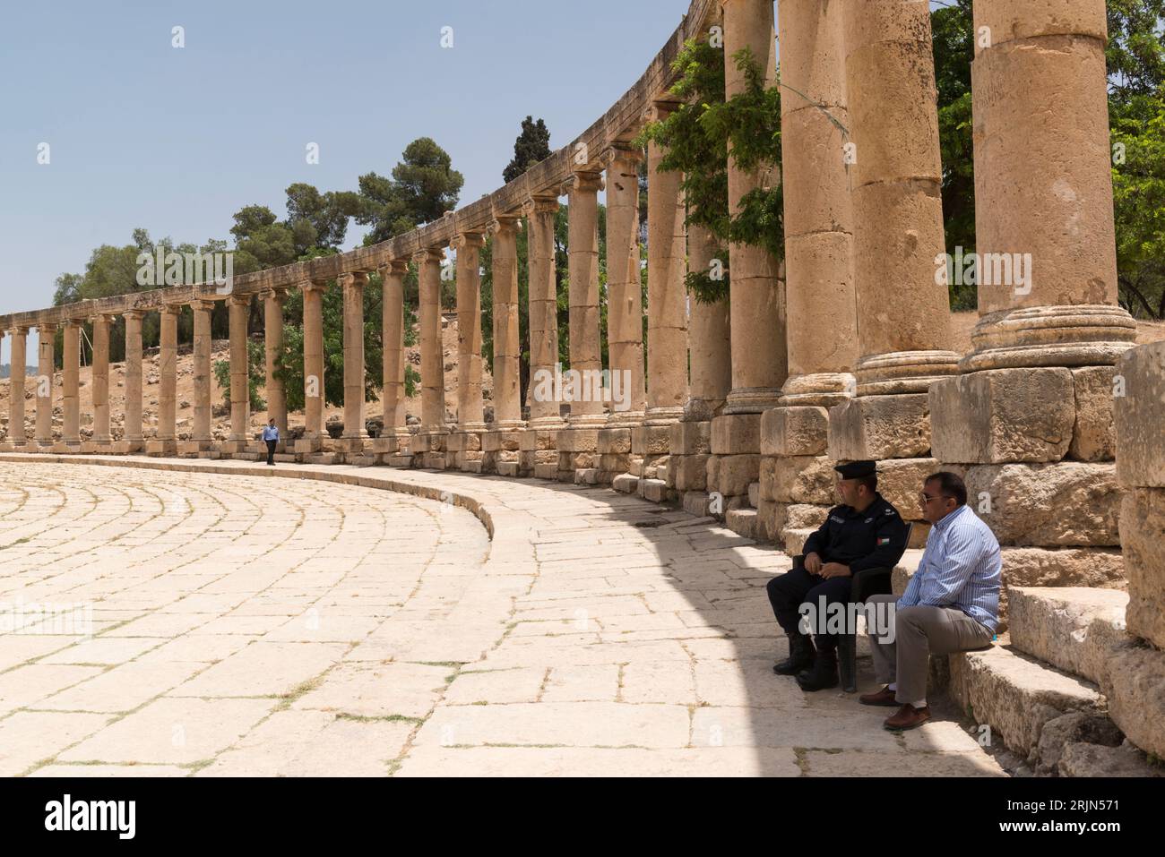 Garde et autre homme assis à l'ombre d'une colonne et surplombant le Forum ovale de l'ancienne ville gréco-romaine Gerasa (Jerash), Jordanie. Banque D'Images