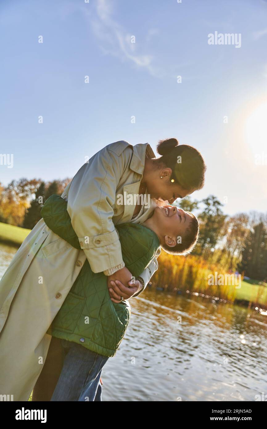 lien familial, amour, mère afro-américaine heureuse et enfant étreinte près du lac, nature, automne, sourire Banque D'Images