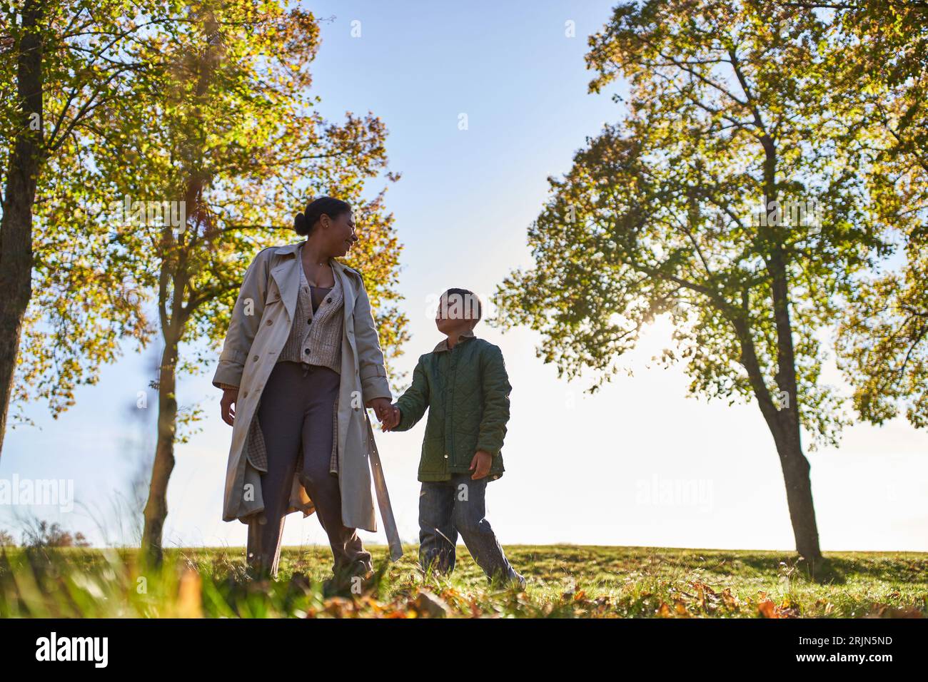 mère et enfant afro-américains tenant la main et marchant près des arbres dans le parc d'automne, saison d'automne Banque D'Images