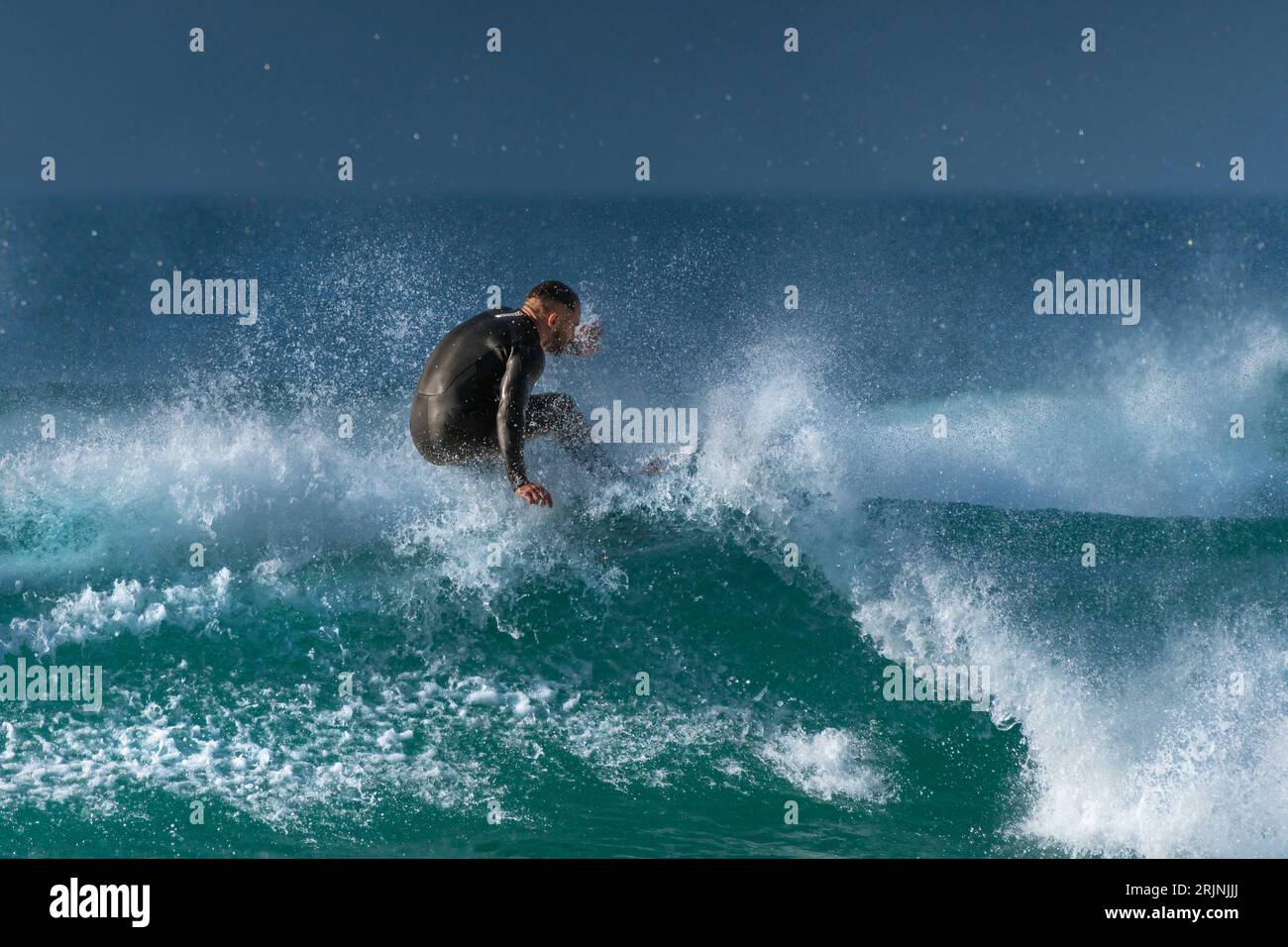 Une action de surf spétaculaire en tant que surfeur mâle fait une vague à Fistral à Newquay, en Cornouailles, en Angleterre, au Royaume-Uni. Banque D'Images