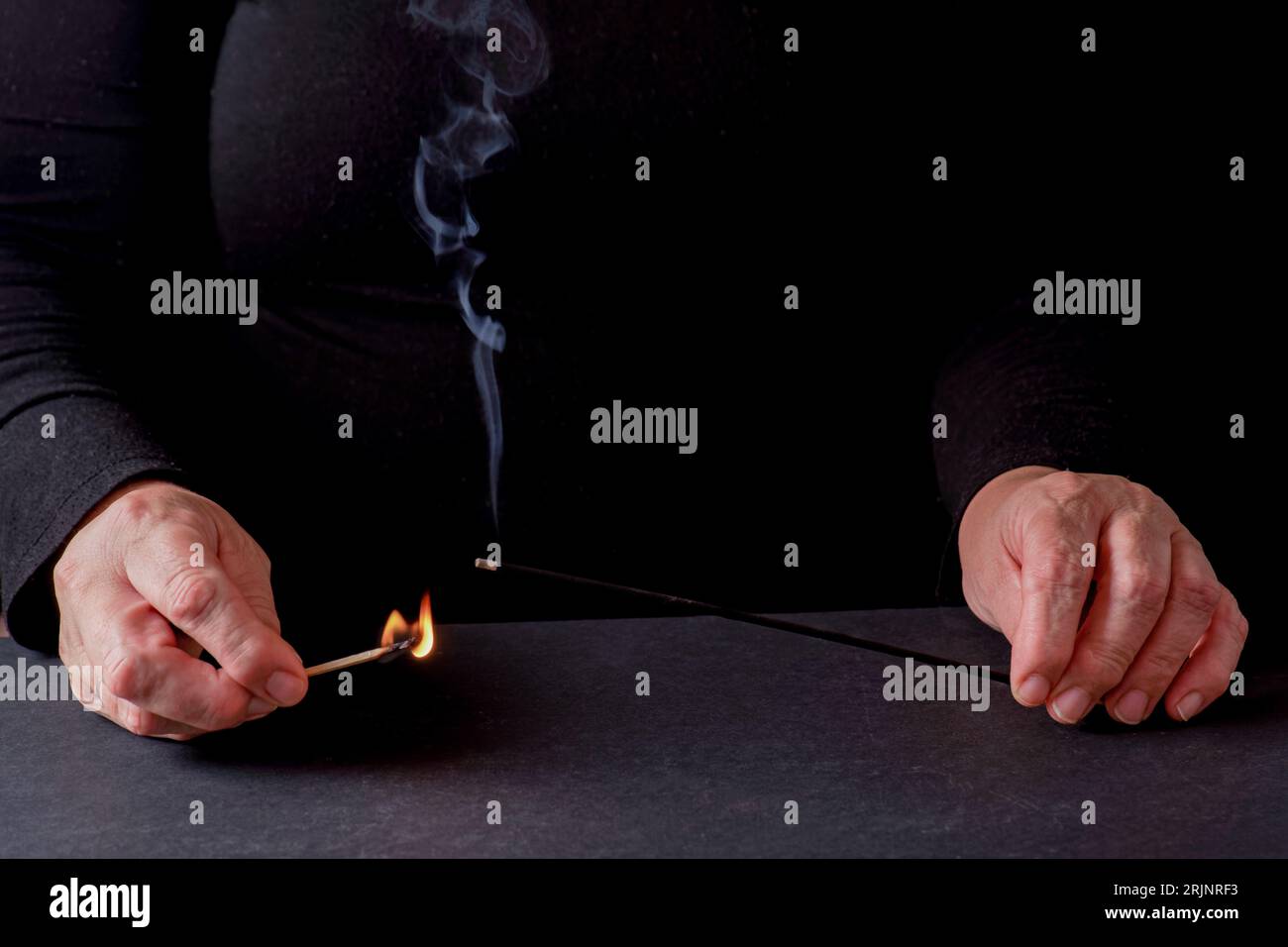 Mains de femme allumant un bâton d'encens avec une allumette avec un fond noir et un espace de copie Banque D'Images