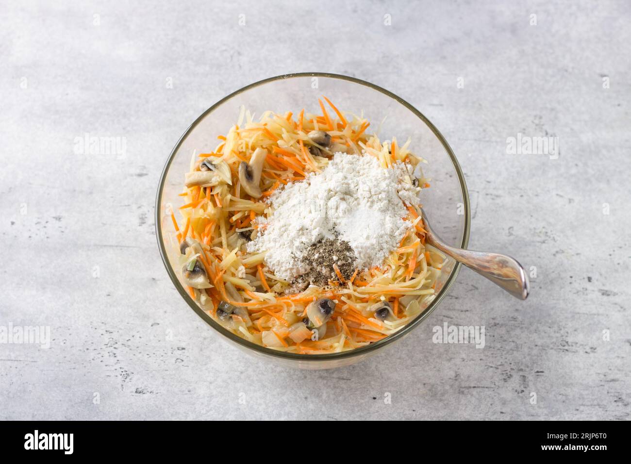 Bol en verre avec mélange de pommes de terre râpées, carottes, œufs, champignons frits avec oignons et farine avec épices pour faire une délicieuse tarte aux pommes de terre, gratin Banque D'Images