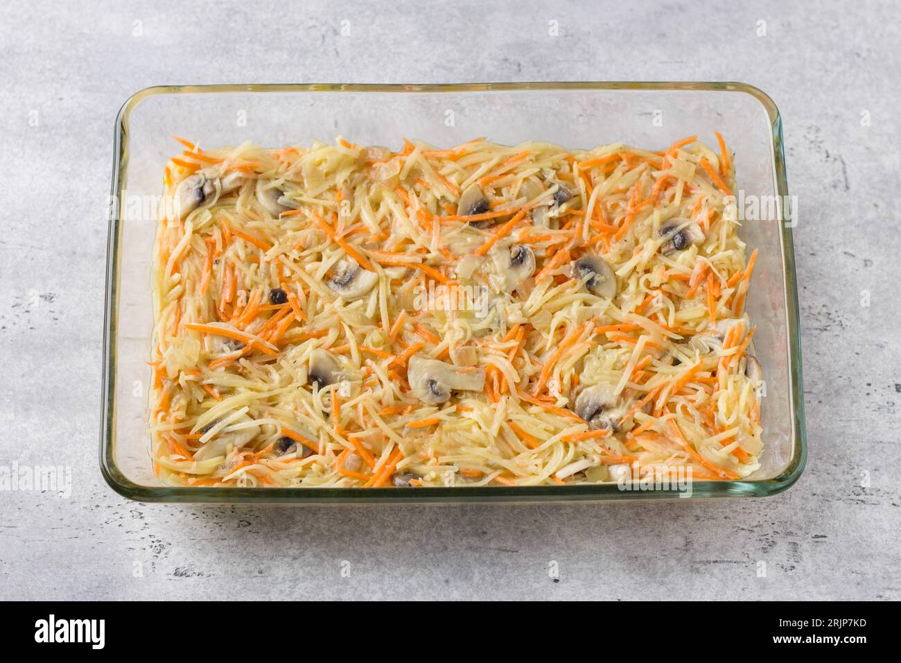 Plat de cuisson en verre avec tarte aux pommes de terre crue, gratin ou cocotte sur fond texturé gris, vue de dessus Banque D'Images