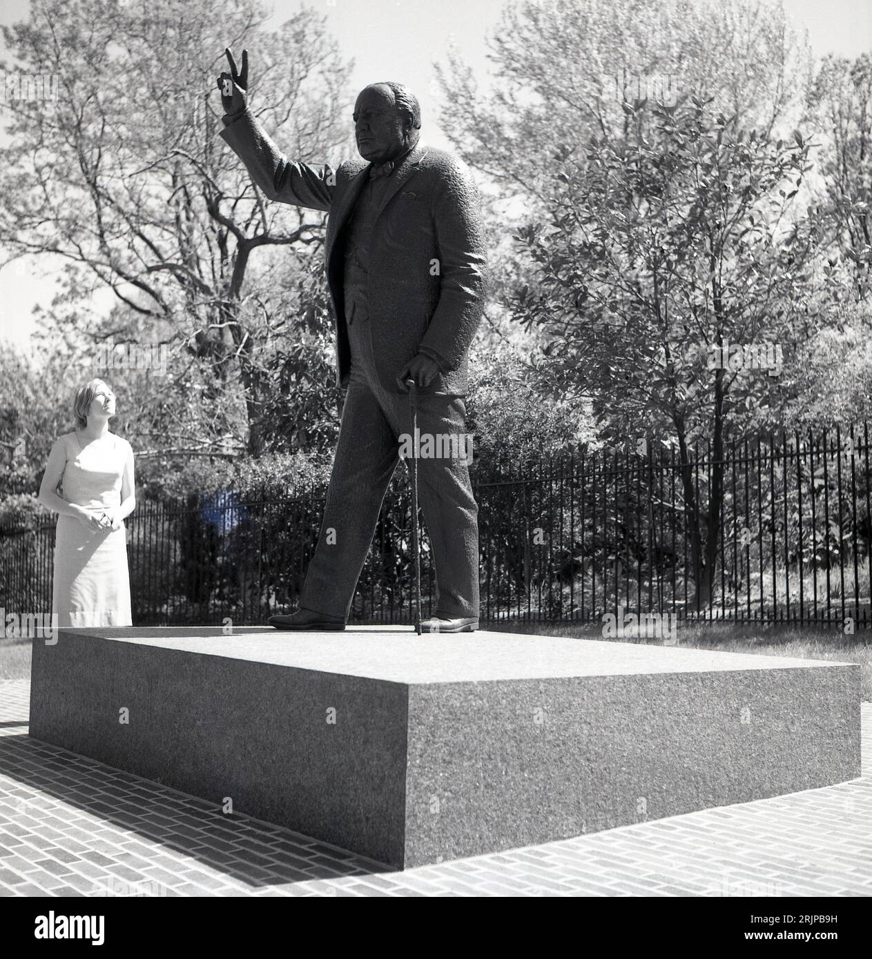 Années 1960, historique, Washington DC, États-Unis, l'été et une dame regardant la sculpture en bronze de Winston Churchill, célèbre Premier ministre de guerre de Grande-Bretagne, montrant son traditionnel signe V pour la victoire. Banque D'Images