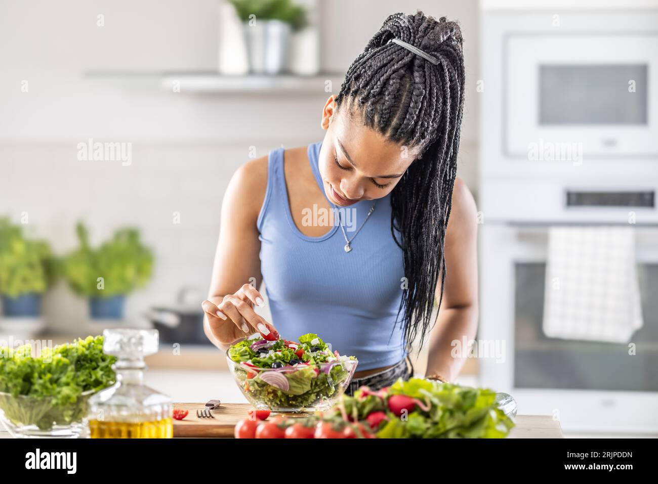 Jeune femme afro-américaine prépare une salade saine, ajoute des tomates. Banque D'Images