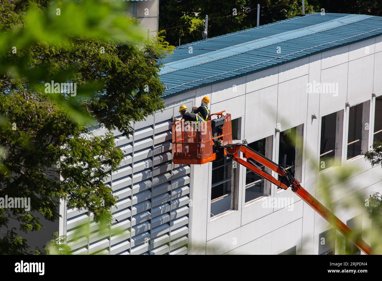 Des ouvriers industriels spécialisés sont soulevés en hauteur par un élévateur à flèche pour effectuer des travaux de réparation sur une structure de bâtiment. Banque D'Images