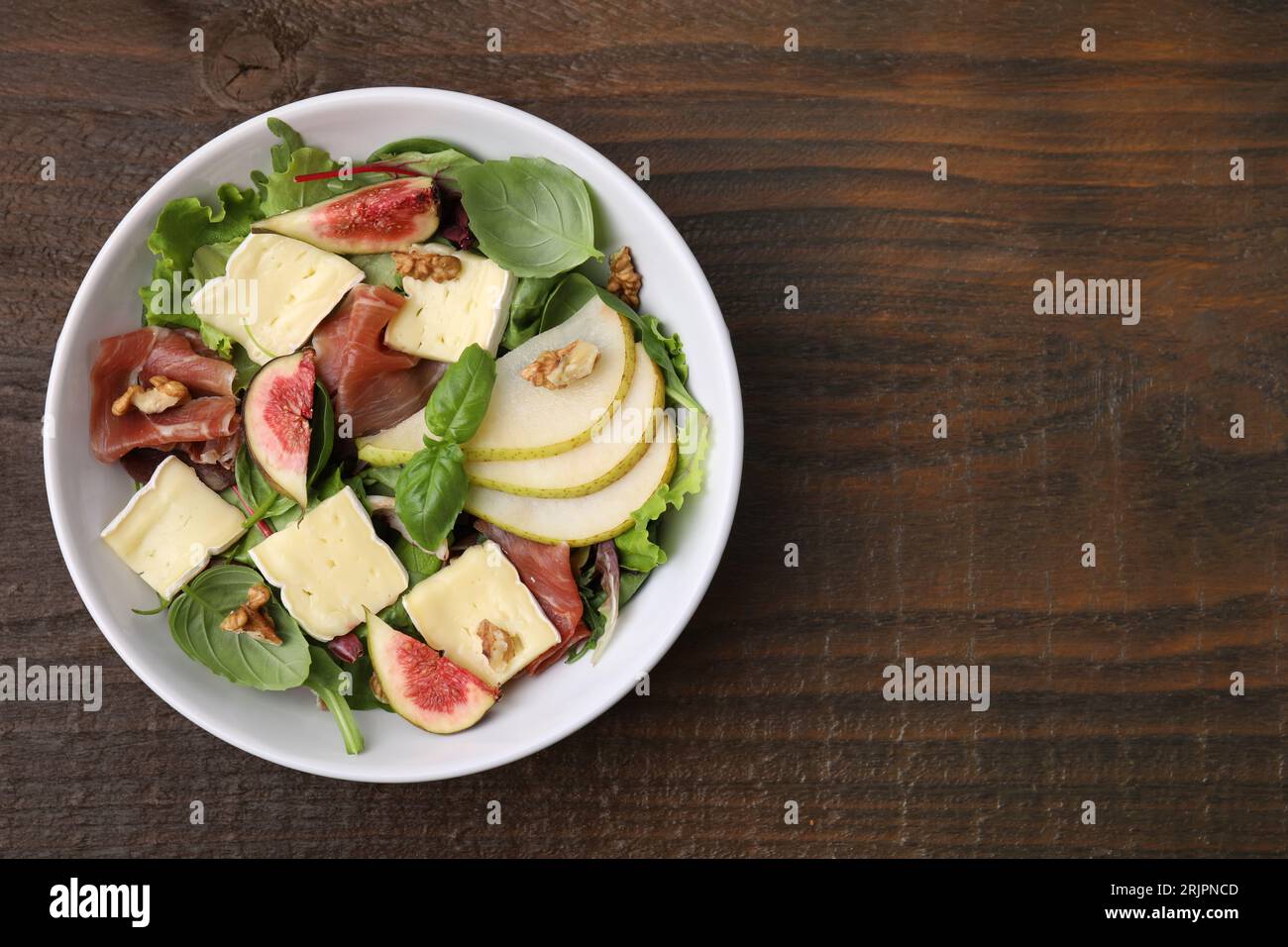 Salade savoureuse avec fromage brie, prosciutto, poire et figues sur table en bois, vue de dessus. Espace pour le texte Banque D'Images
