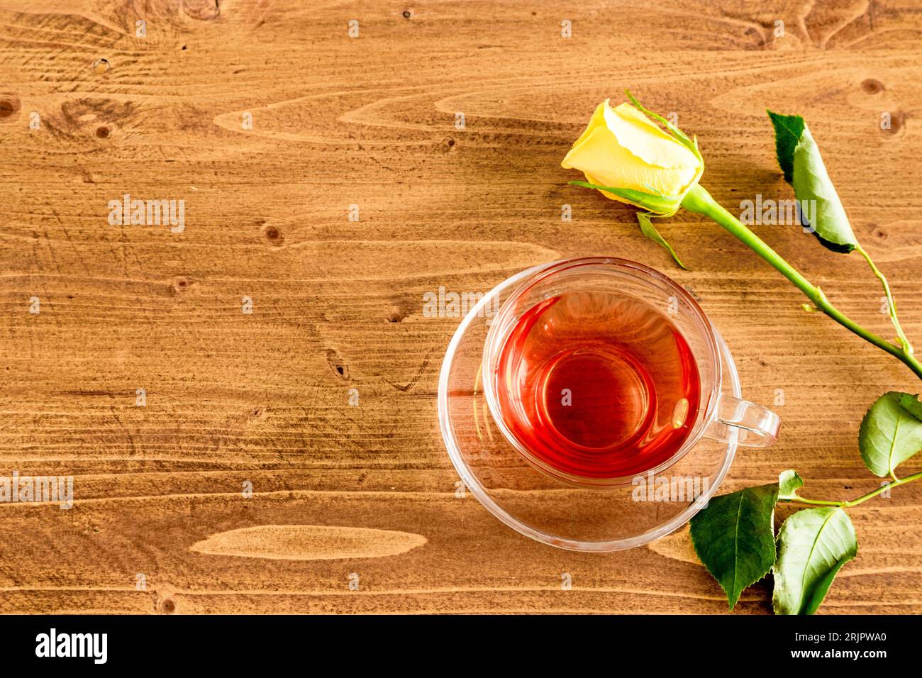 Une vue de dessus d'une rose jaune et une tasse de thé noir dans une tasse en verre transparent sur une table en bois. Banque D'Images