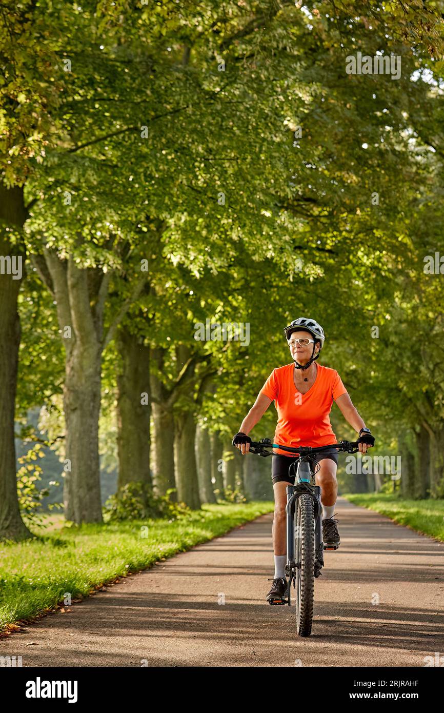 Sénior femme sénior attrayante à vélo avec son vélo de montagne électrique dans une belle avenue de chêne et châtaignier à Ludwigsburg, Baden-Wuerttemberg, GE Banque D'Images