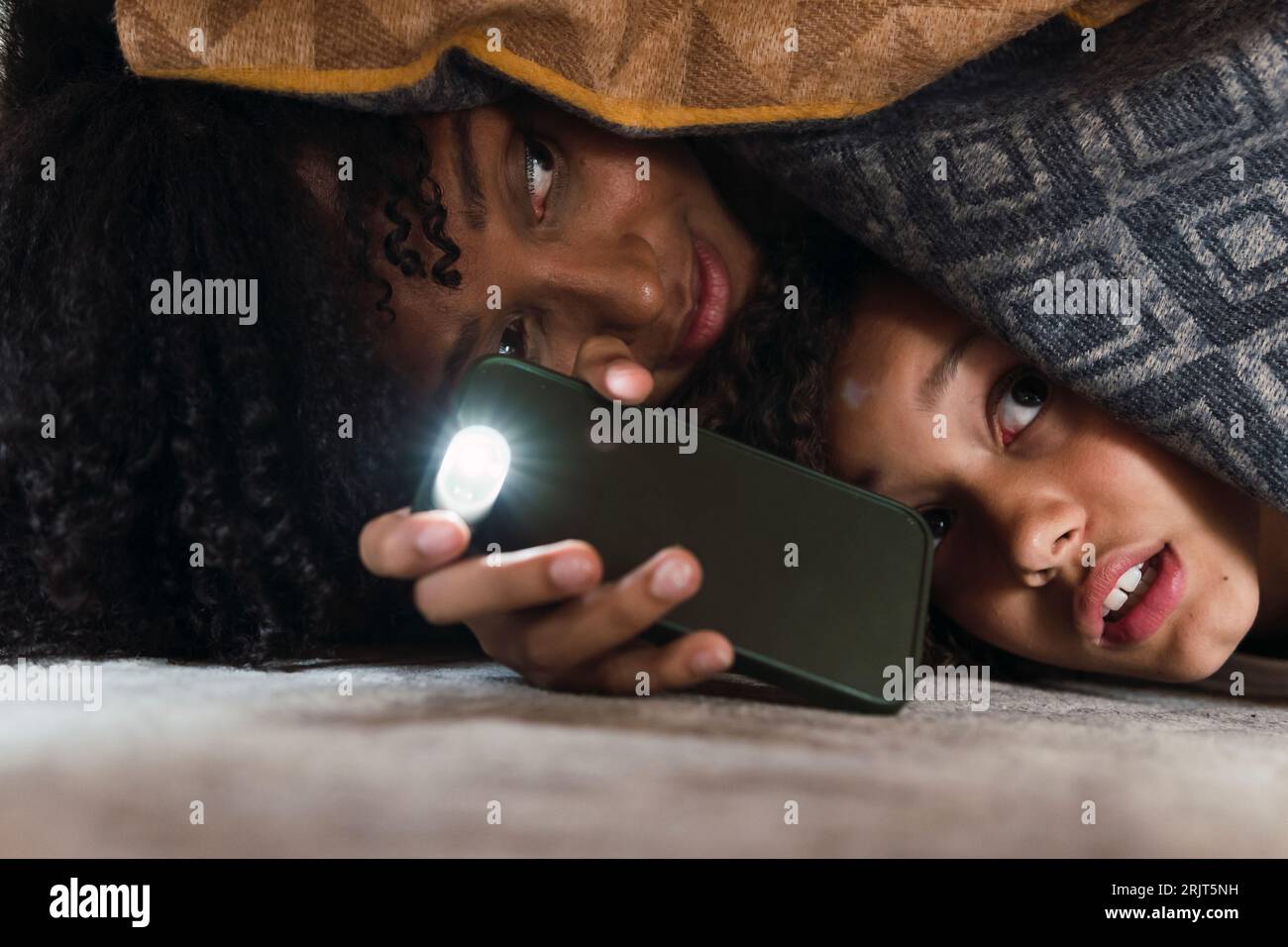 Mère et fille effrayées cherchant le sol sous le canapé avec la torche de smartphone Banque D'Images