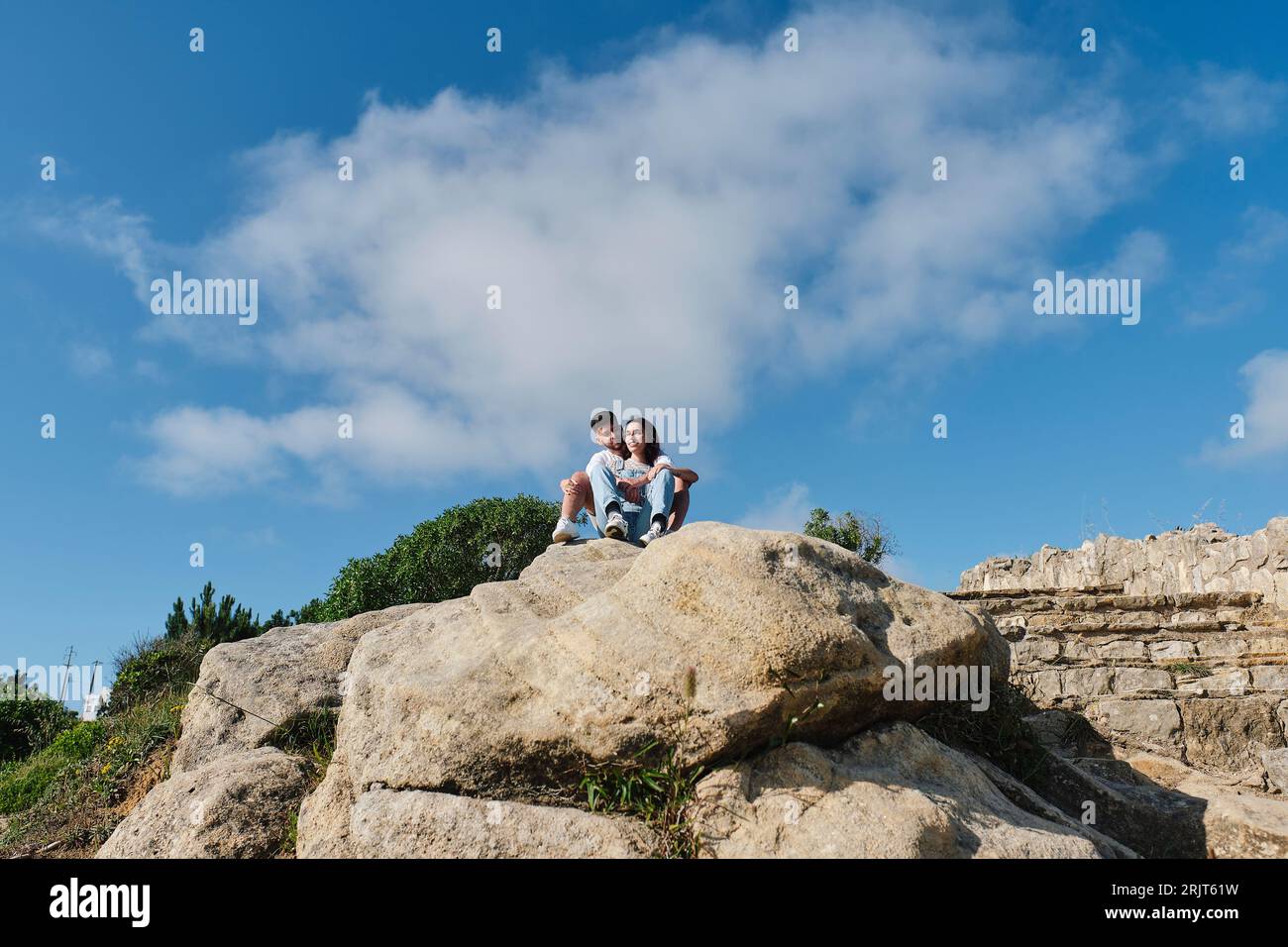 Jeune couple assis sur des rochers sous le ciel Banque D'Images