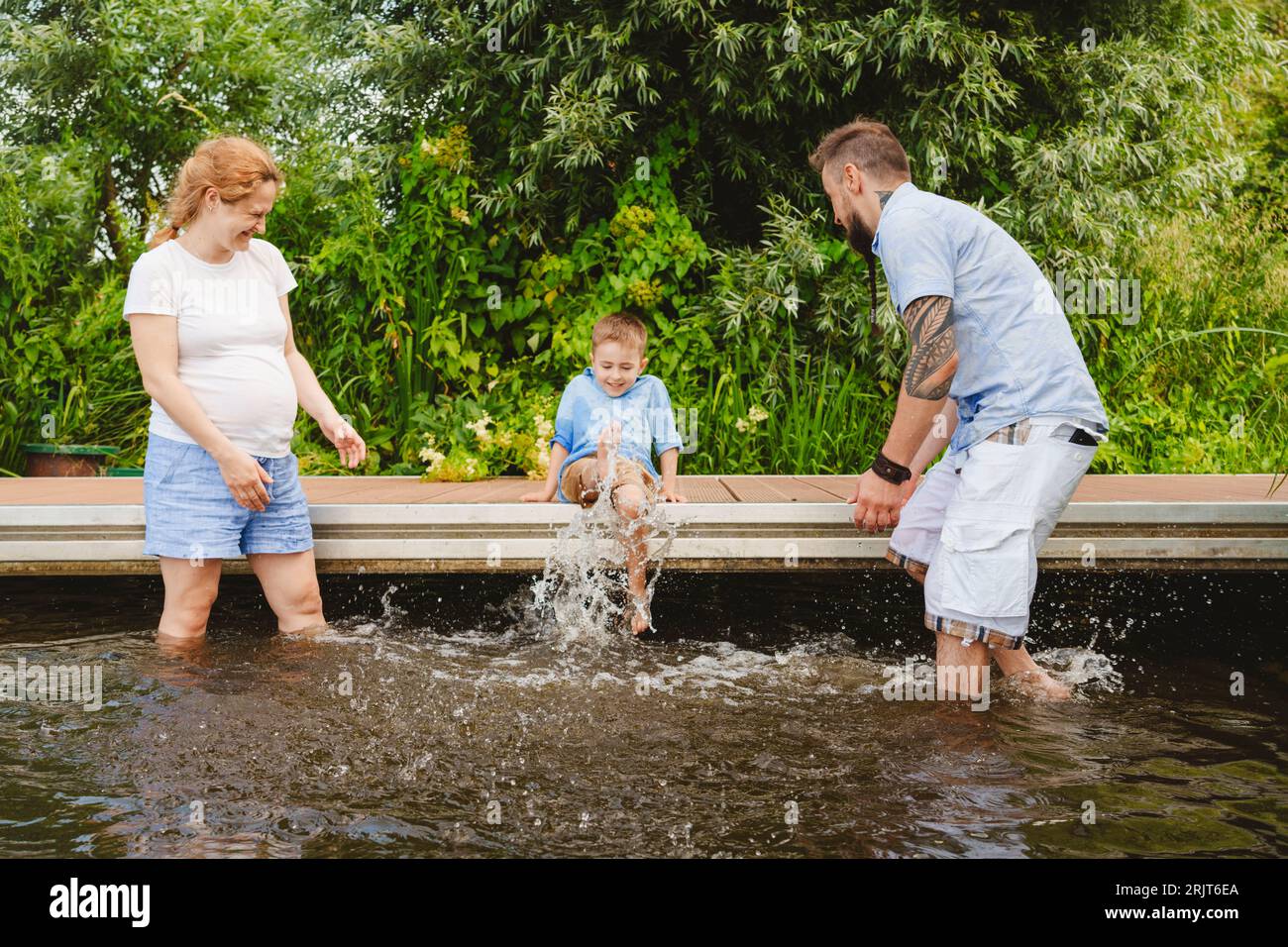 Garçon éclaboussant de l'eau avec les parents appréciant dans le lac Banque D'Images