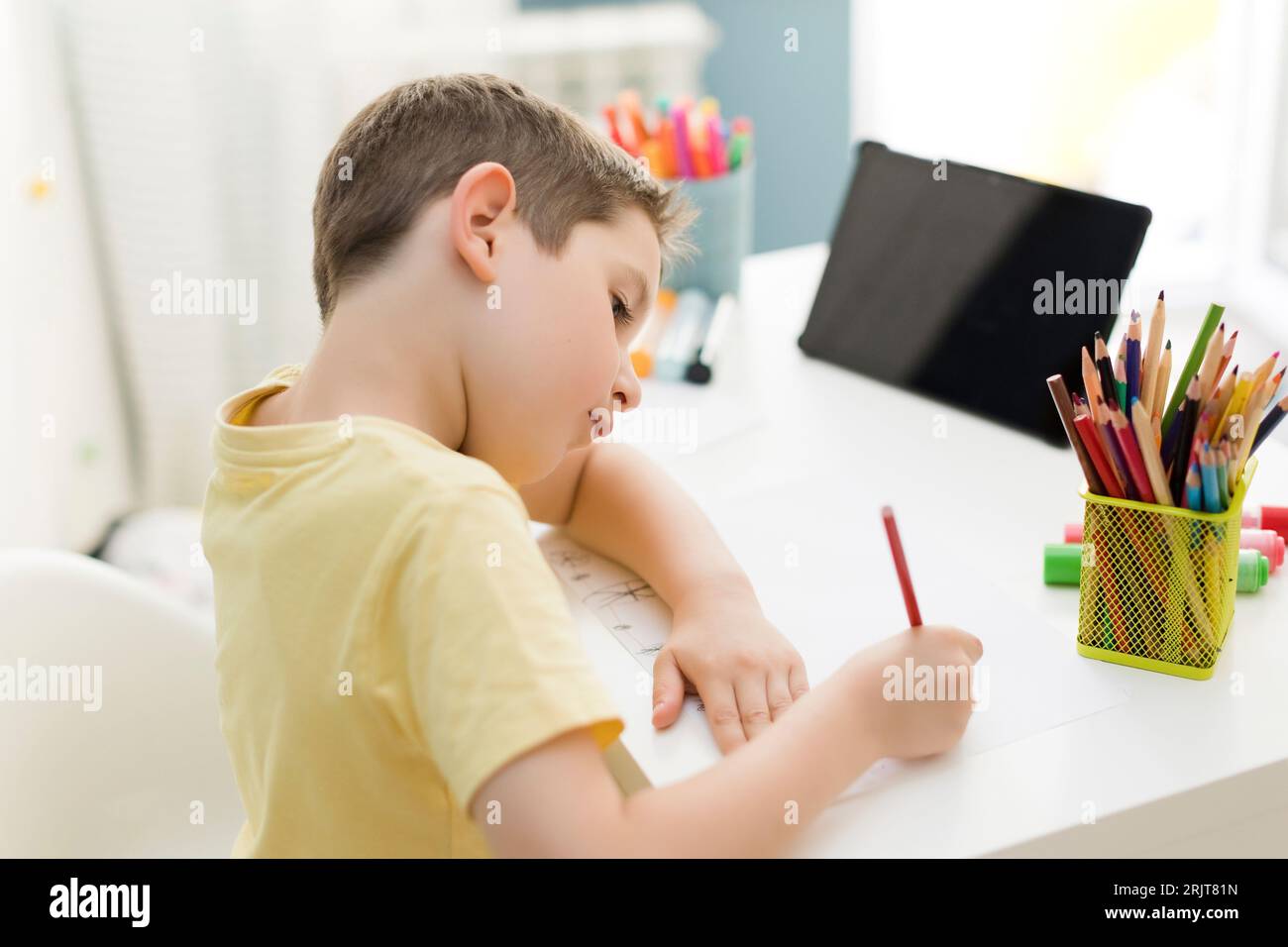 Dessin de garçon souriant avec un crayon de couleur près de la tablette pc à la maison Banque D'Images