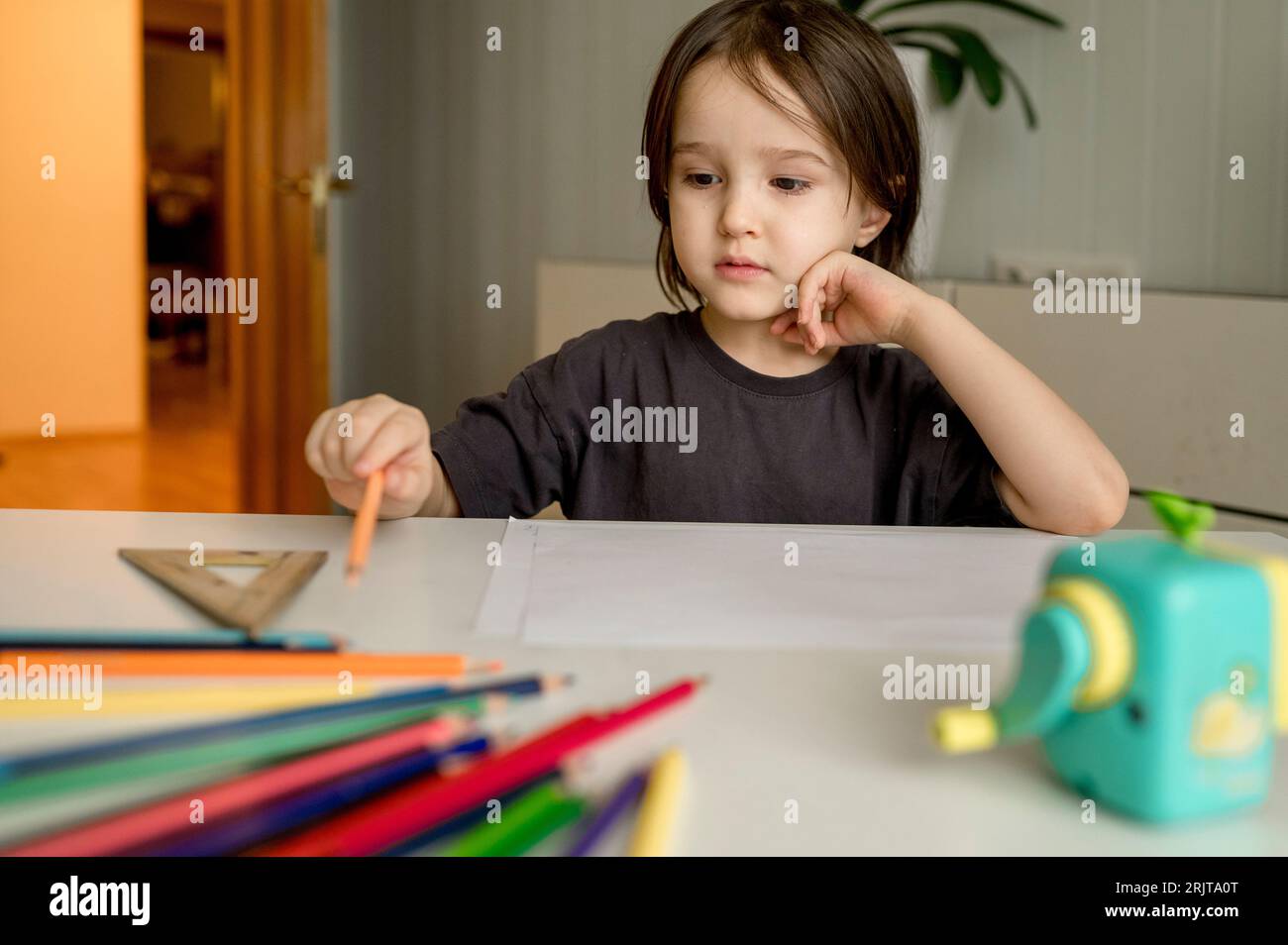 Garçon réfléchi avec des crayons de couleur sur la table à la maison Banque D'Images