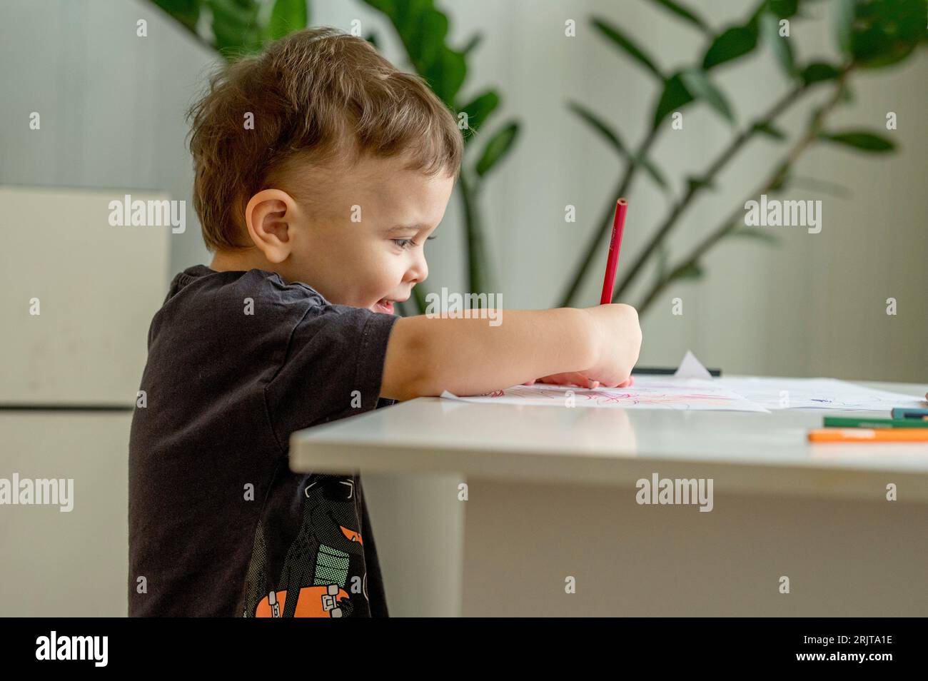 Souriant garçon coloriant sur papier assis à la maison Banque D'Images
