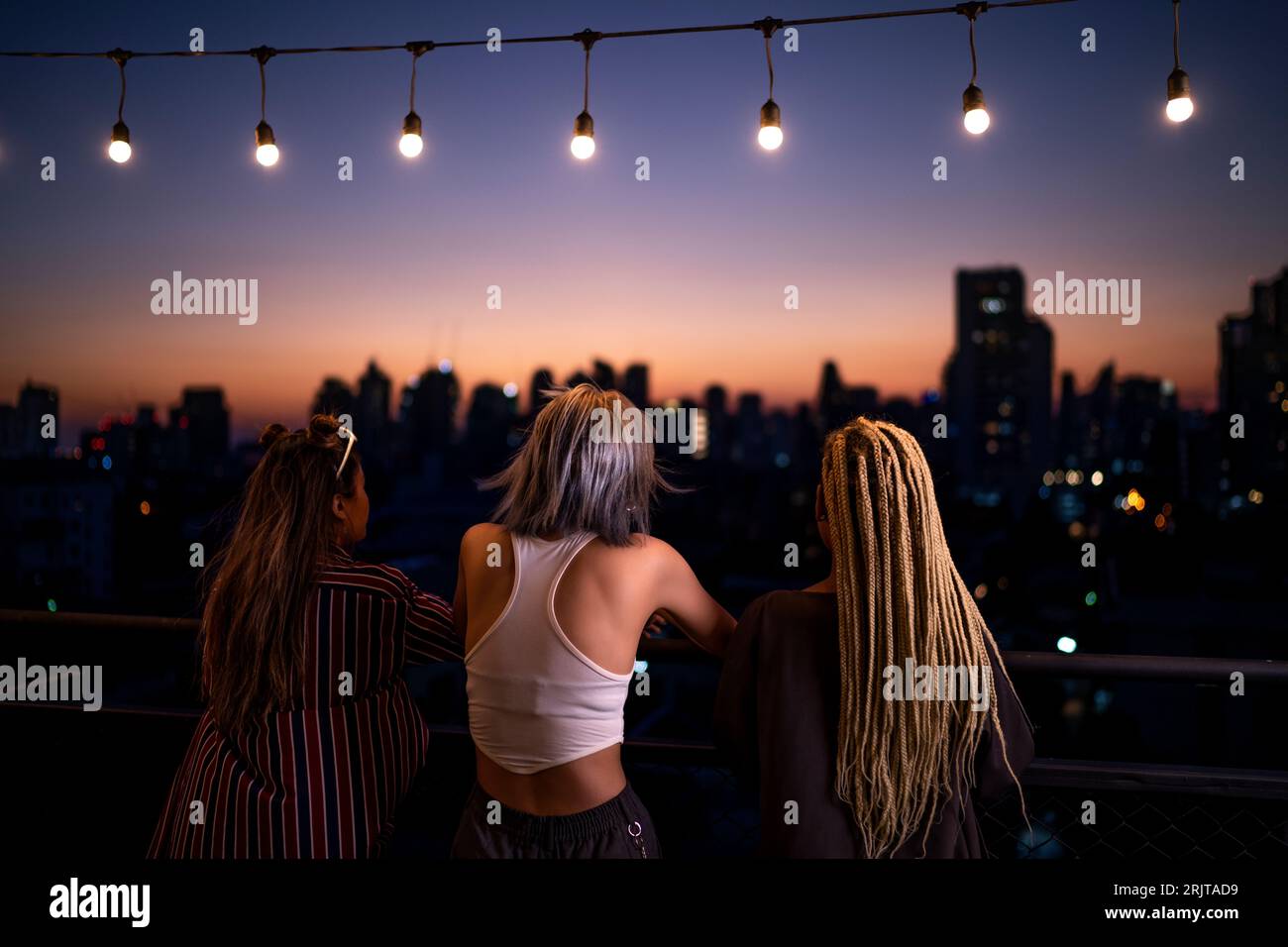 Amis debout sous les guirlandes lumineuses sur le toit au crépuscule Banque D'Images