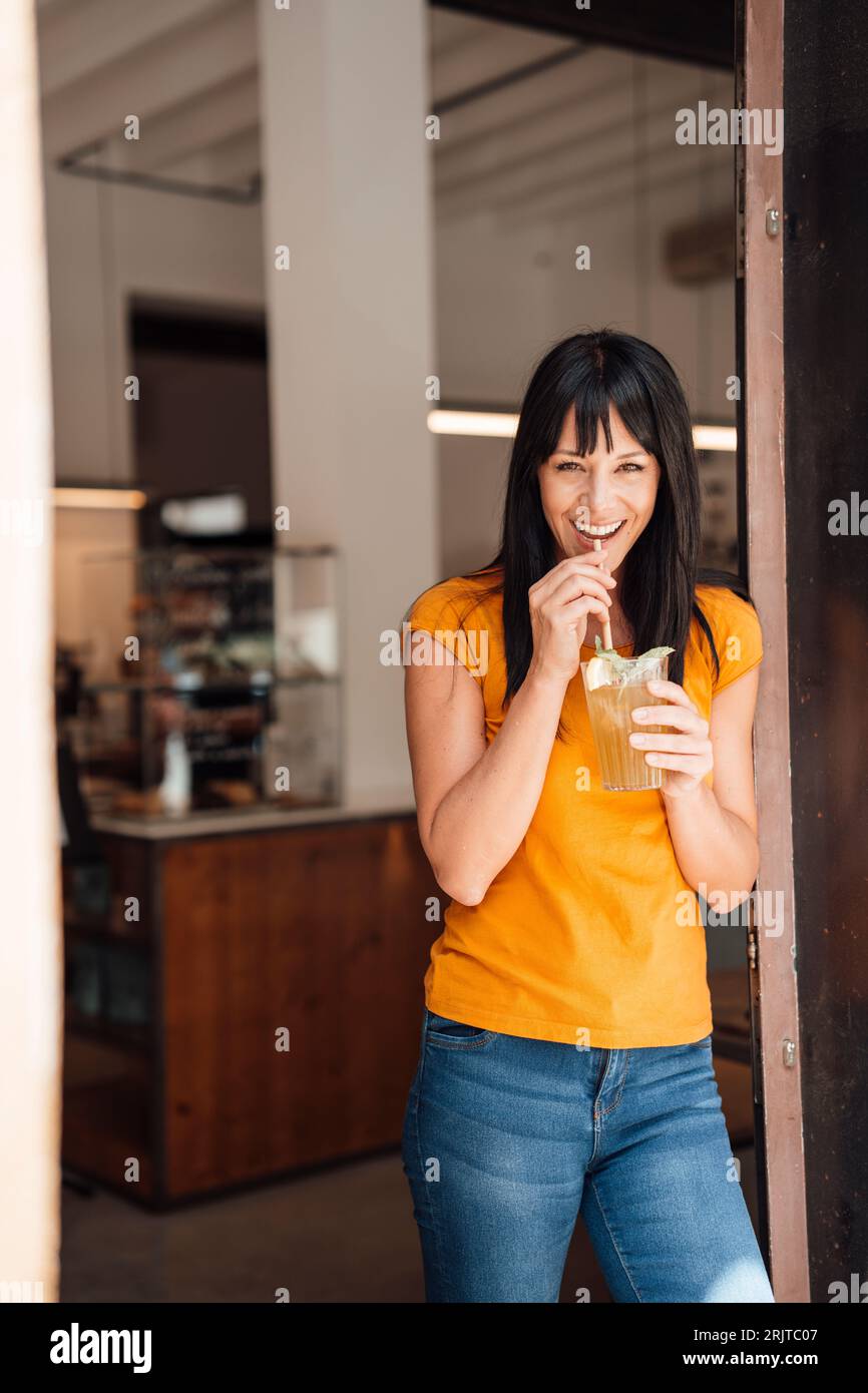 Heureuse femme mature buvant du jus dans la porte de café Banque D'Images