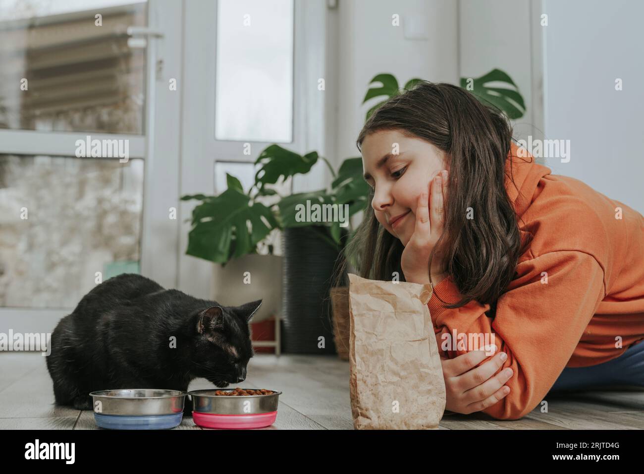 Fille souriante regardant le chat manger de la nourriture à la maison Banque D'Images