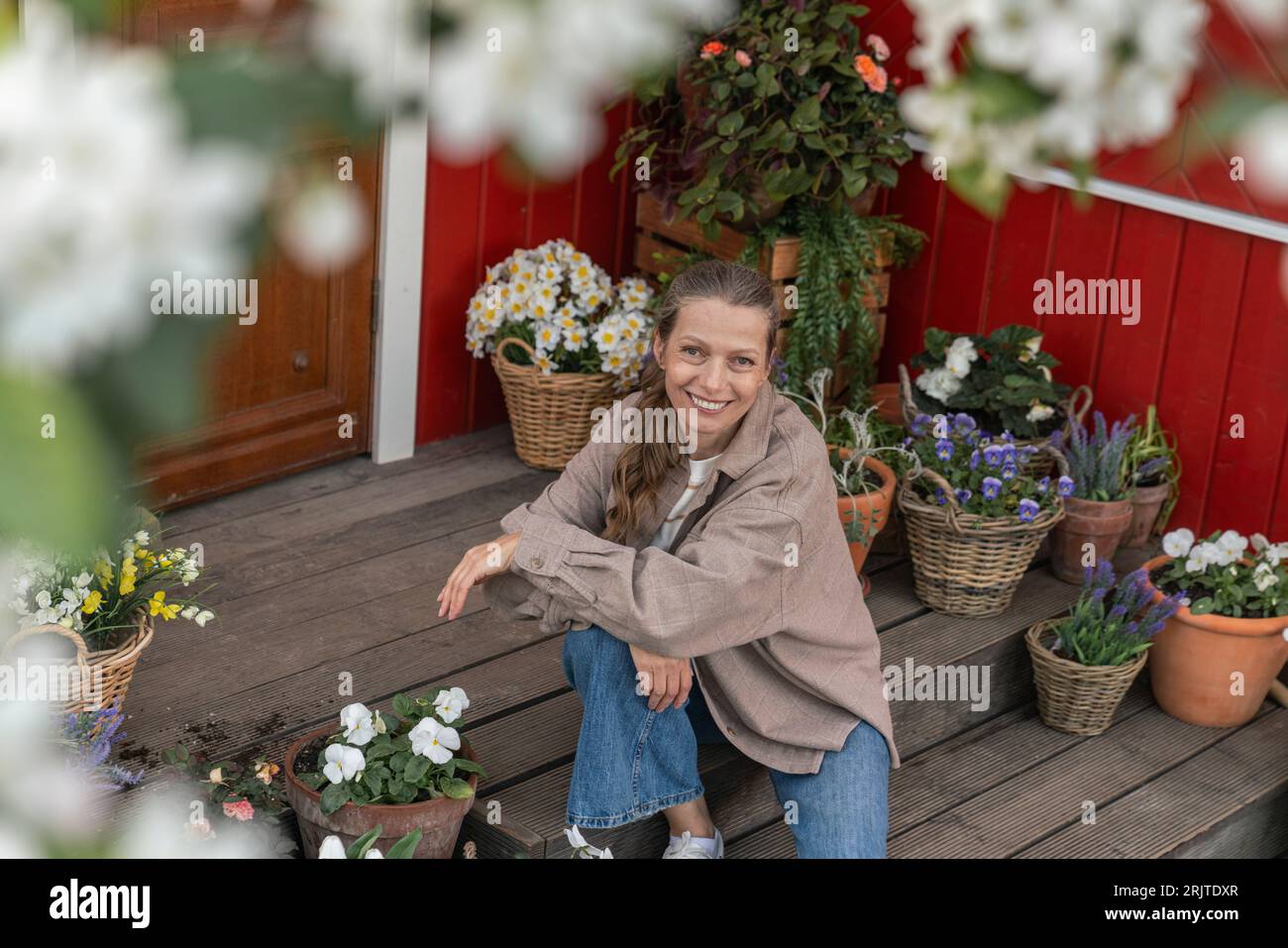 Femme mature souriante assise par des plantes à fleurs sur le porche Banque D'Images