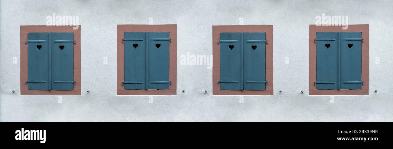 Fenêtres avec volets en bois fermés bleus sur fond de mur en pierre blanche. Obturateur avec trou de coeur, symbole d'amour. Banque D'Images